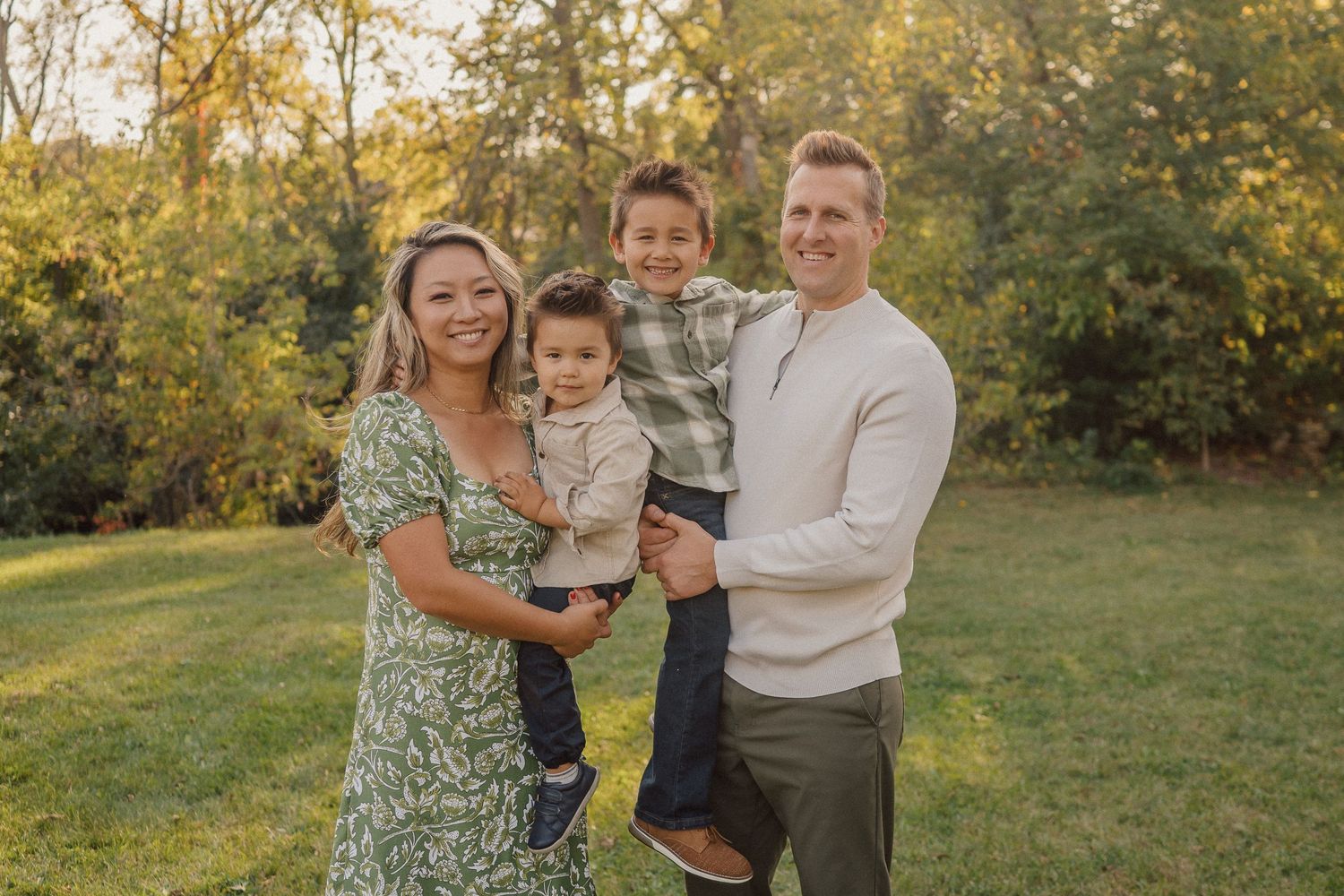 A family in casual attire poses together on a grassy field during golden hour in autumn.