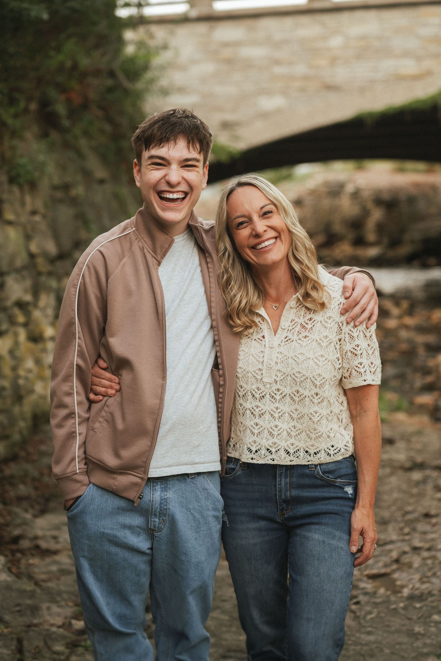 Couple in casual outfits posing together outdoors against stone wall background in natural lighting.
