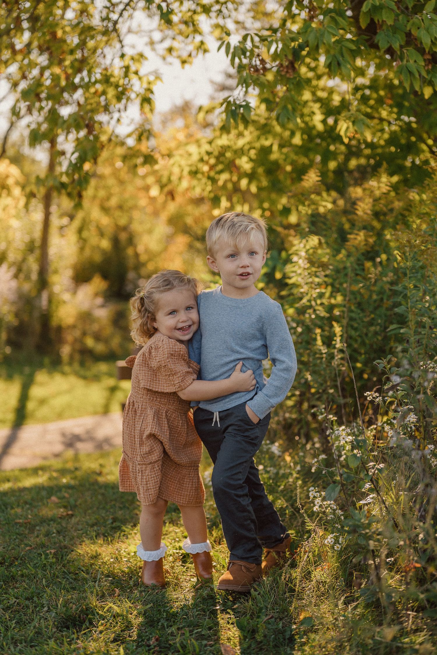 Two children playing together among flowering bushes in a sunlit garden.