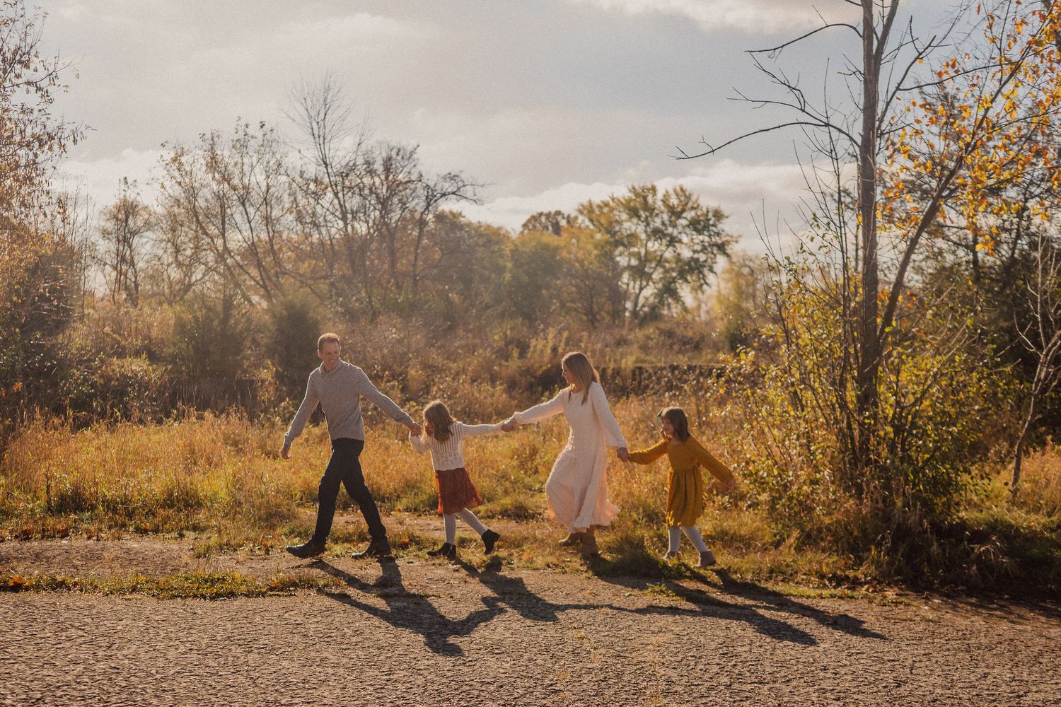 Silhouettes of people playing and jumping together in a golden autumn field at sunset with long shadows cast.