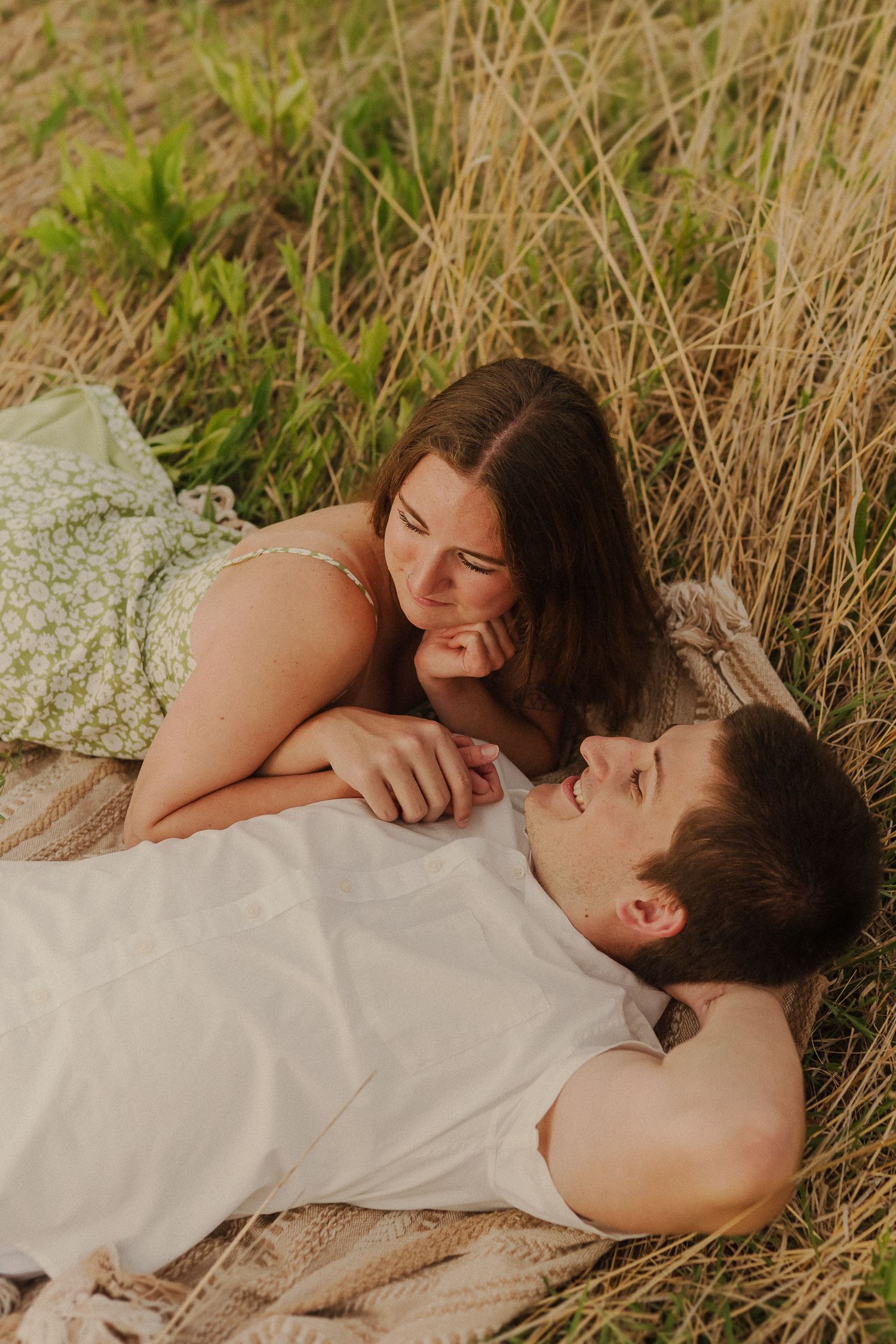 A couple laying together on a blanket in tall grass during golden hour.
