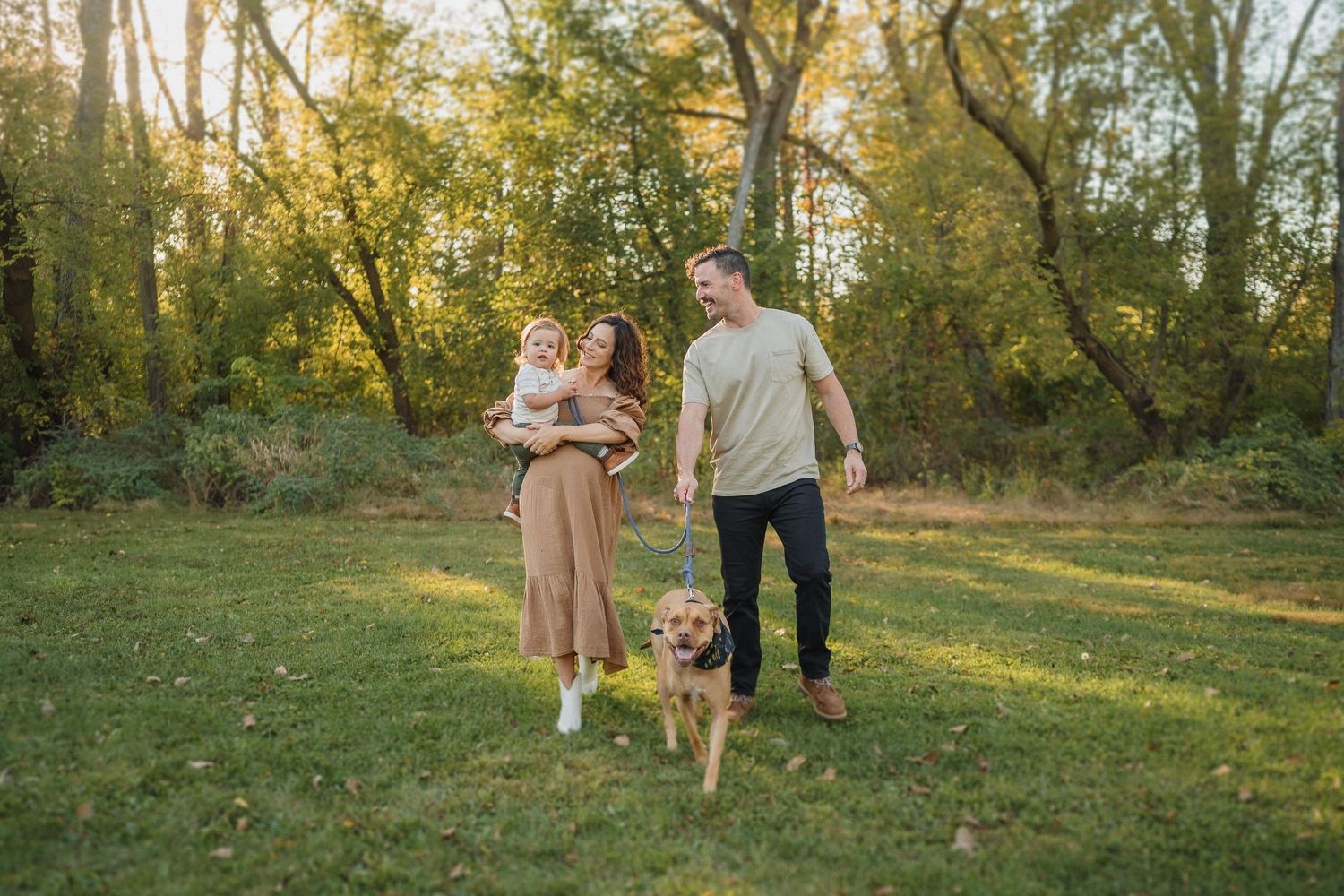 Family walks their dog in a sunlit park during golden hour.