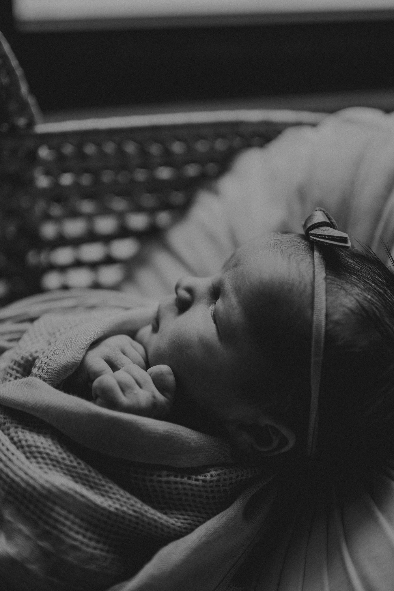 Black and white portrait of sleeping newborn with bow accessory on textured surface.