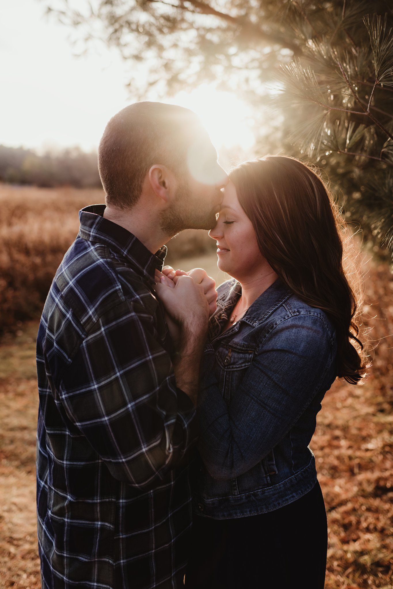 Couple in casual attire sharing tender moment at sunset in outdoor setting.