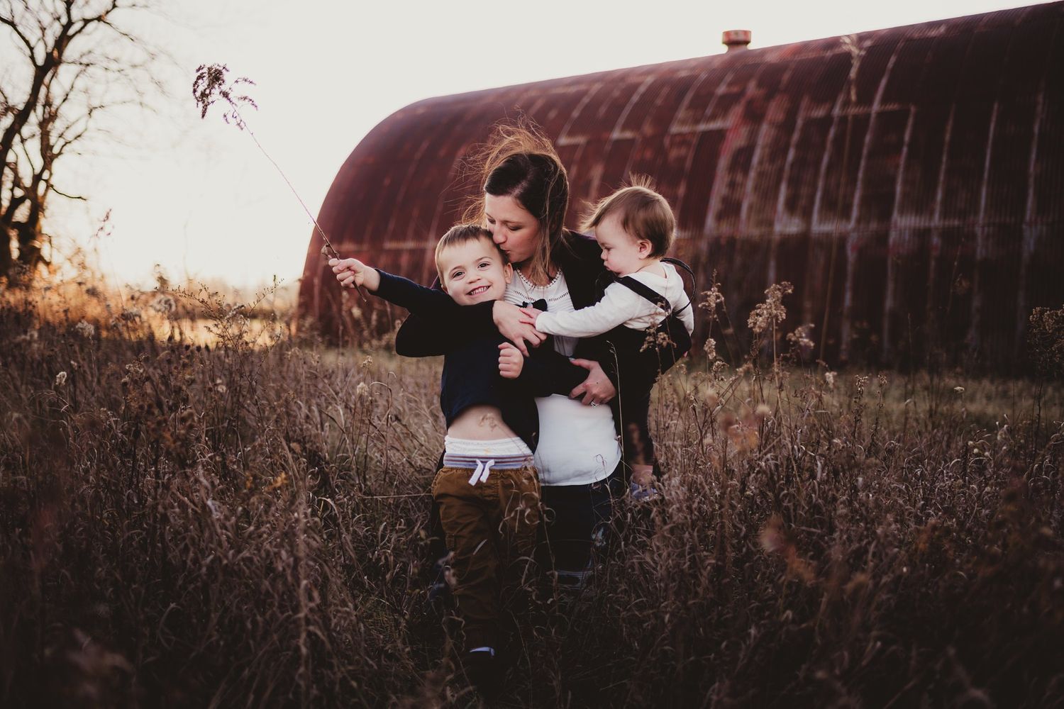 Family enjoys a playful moment together in a field with an old barn in the background.