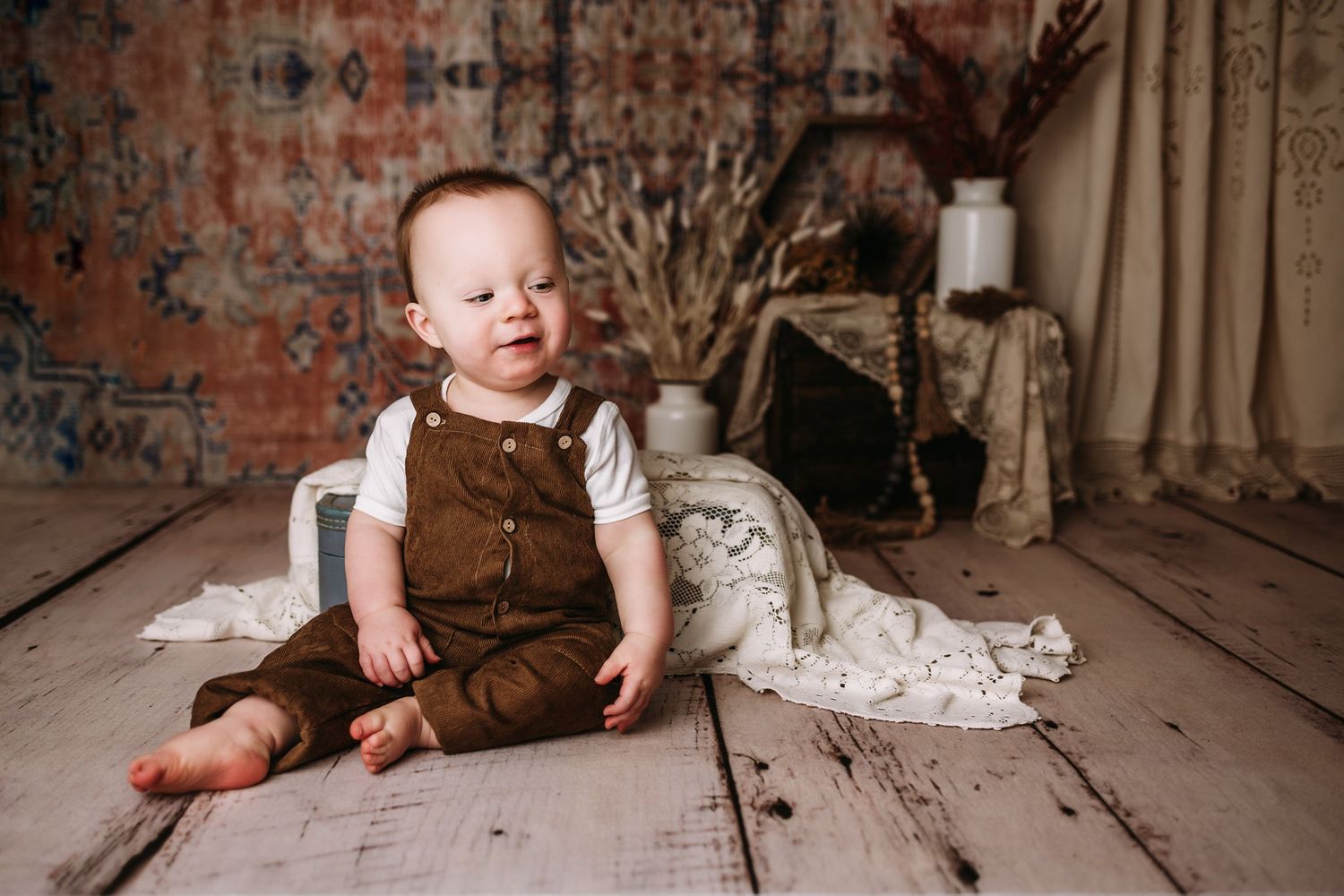 Brown overalls and white shirt outfit in vintage brick wall setting with fabric backdrop and wooden floor.