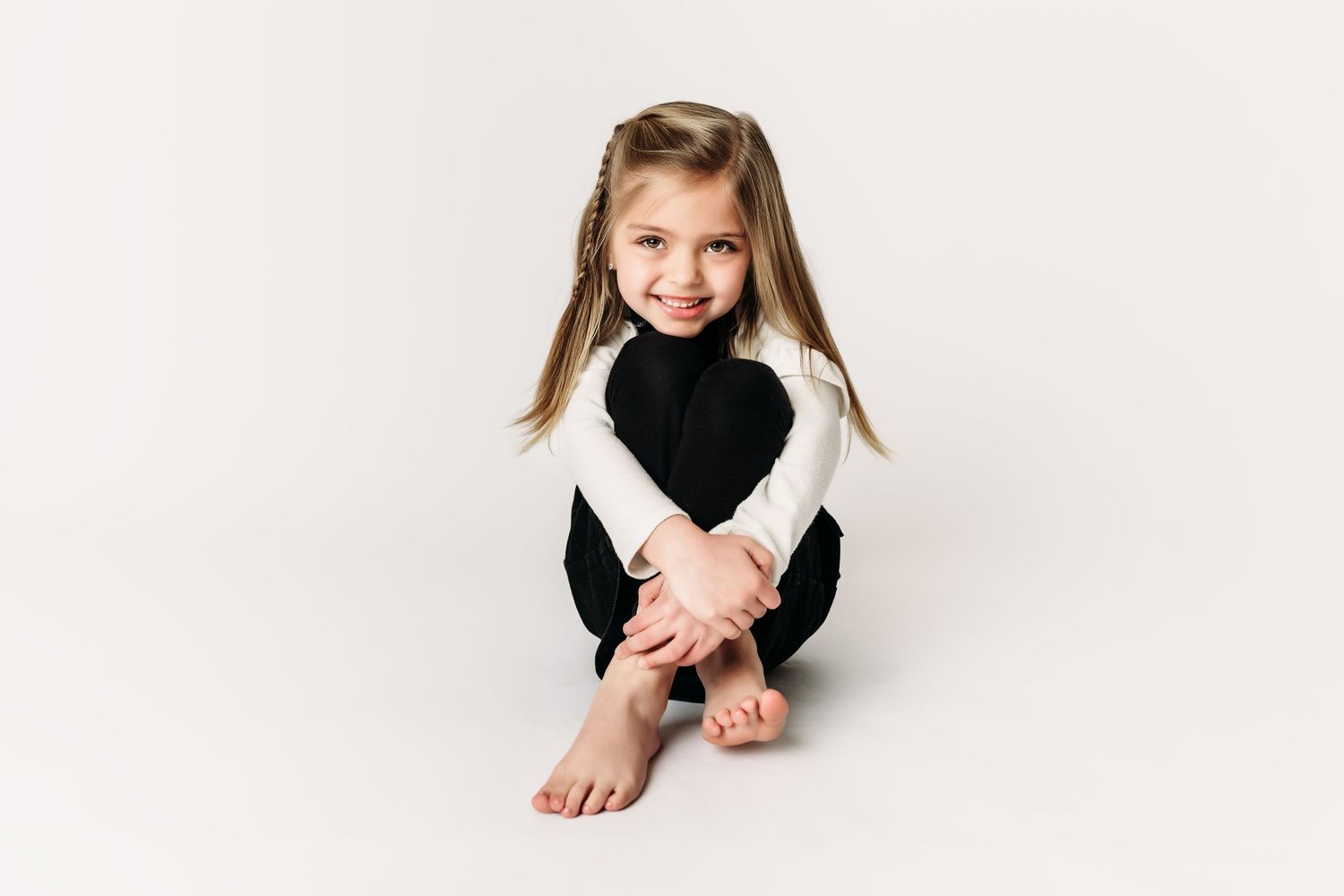Child in black and white outfit sitting cross-legged on white background.