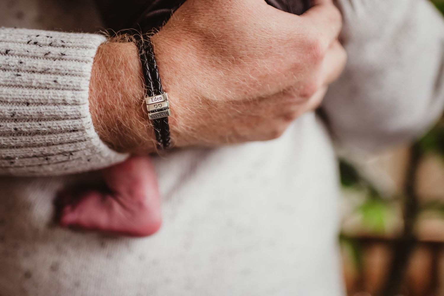 Close-up detail of hands wearing cream sweater and wristwatch while holding infant.