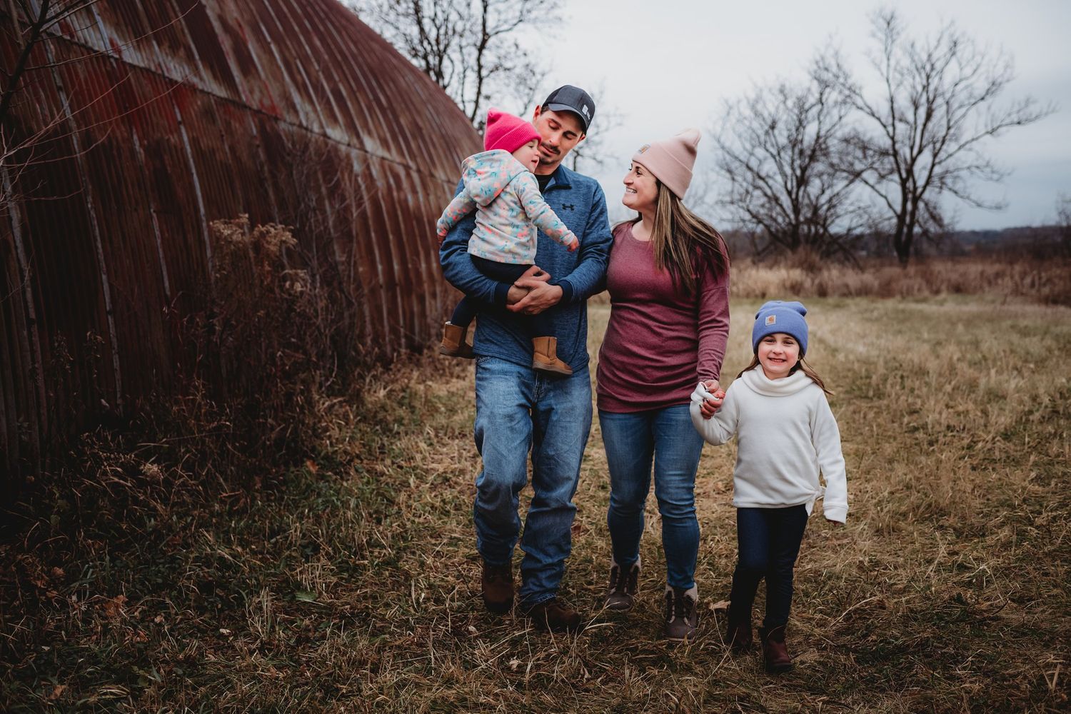 Casual family portrait in winter clothing against weathered red barn structure.