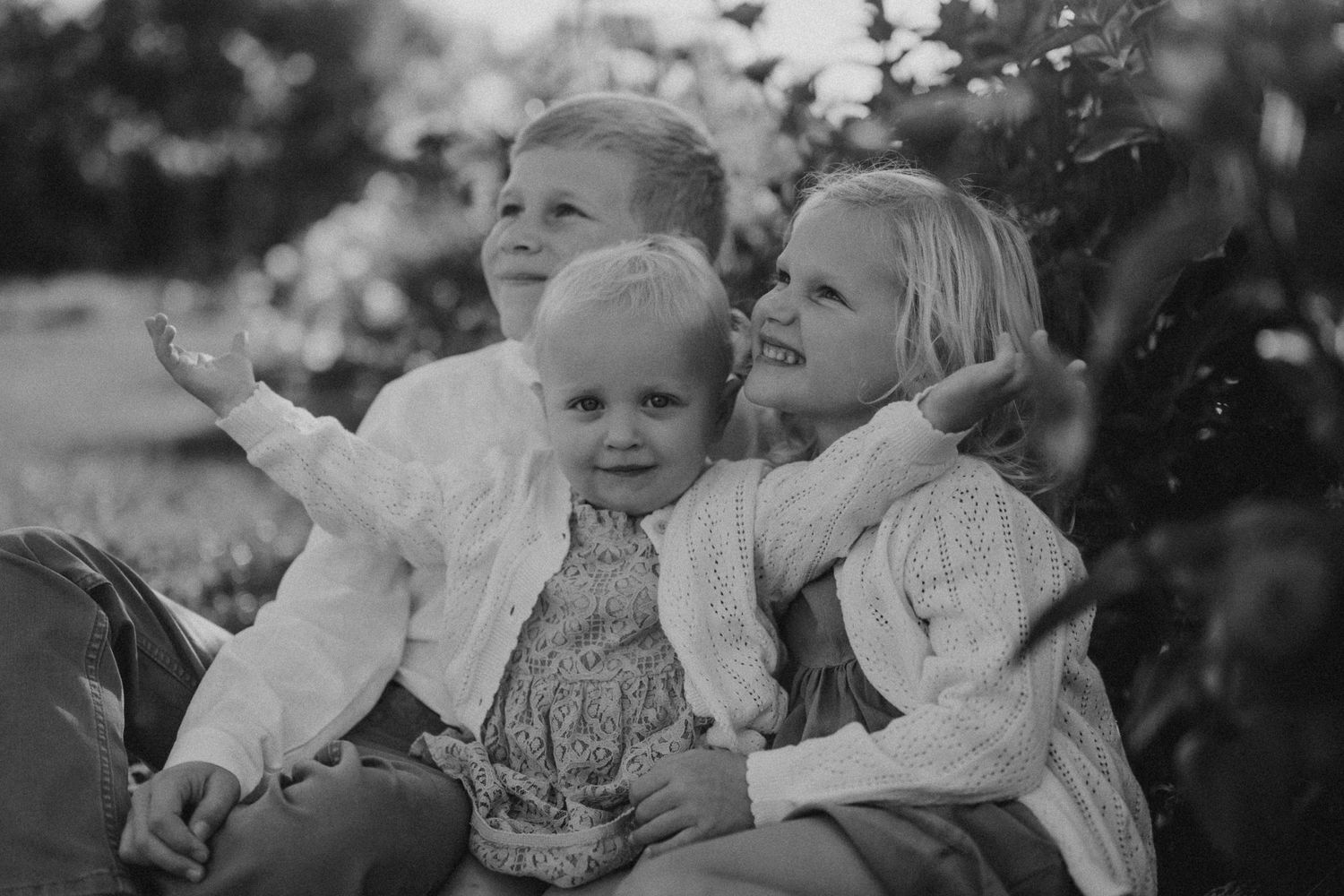 A black and white portrait of three people sitting close together outdoors.