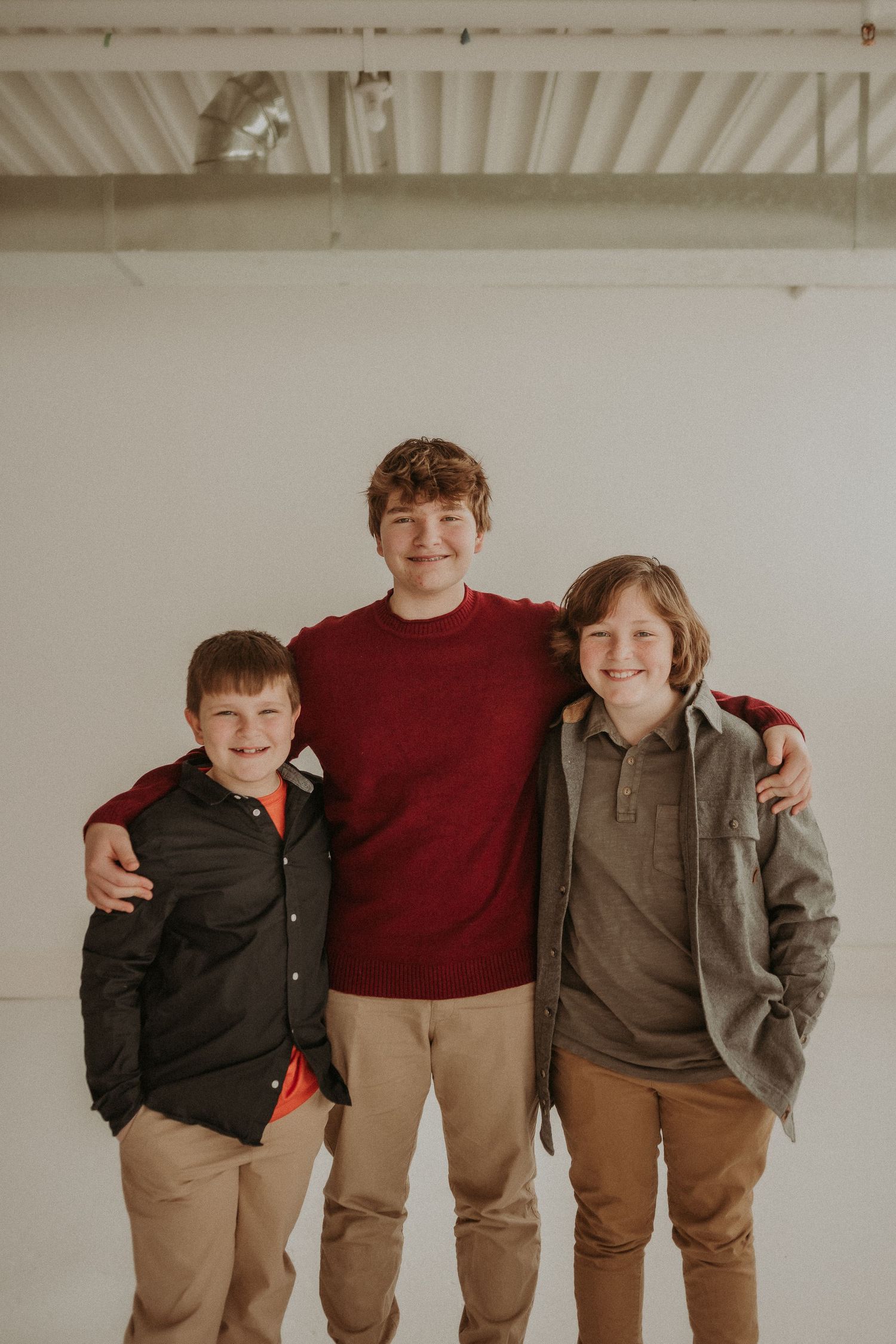 Three siblings in coordinating casual wear pose against white studio backdrop.