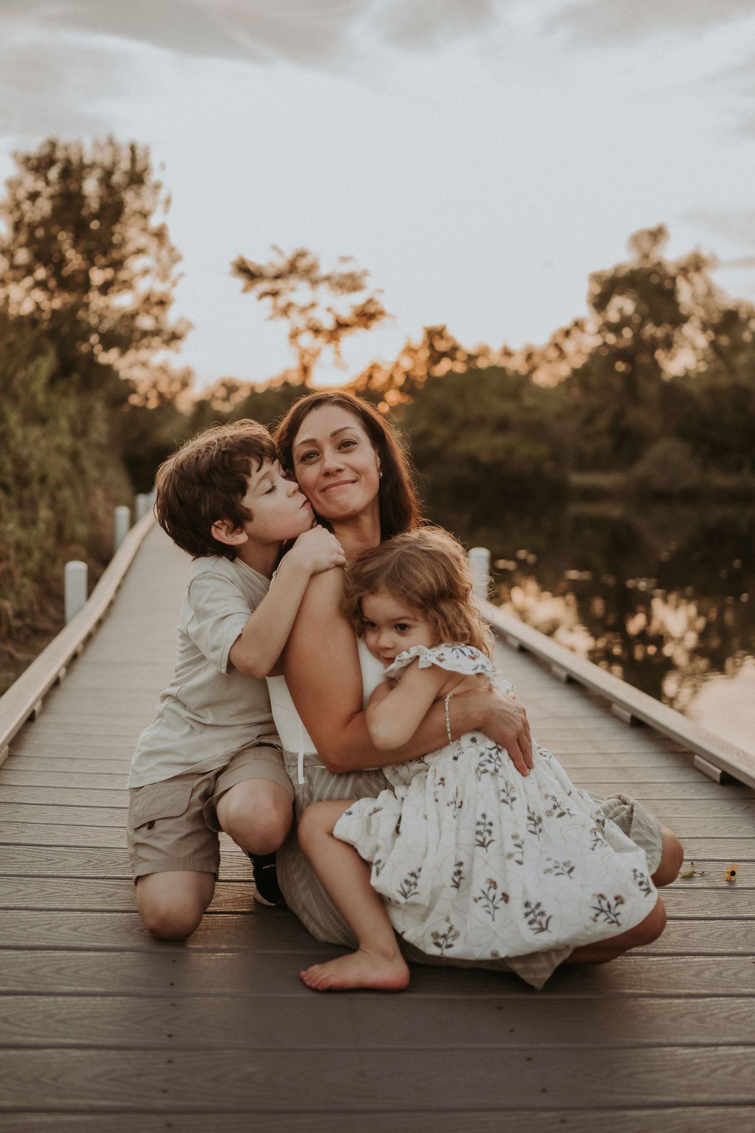 Sweet candid moment of family affection captured on a lakeside boardwalk at sunset.