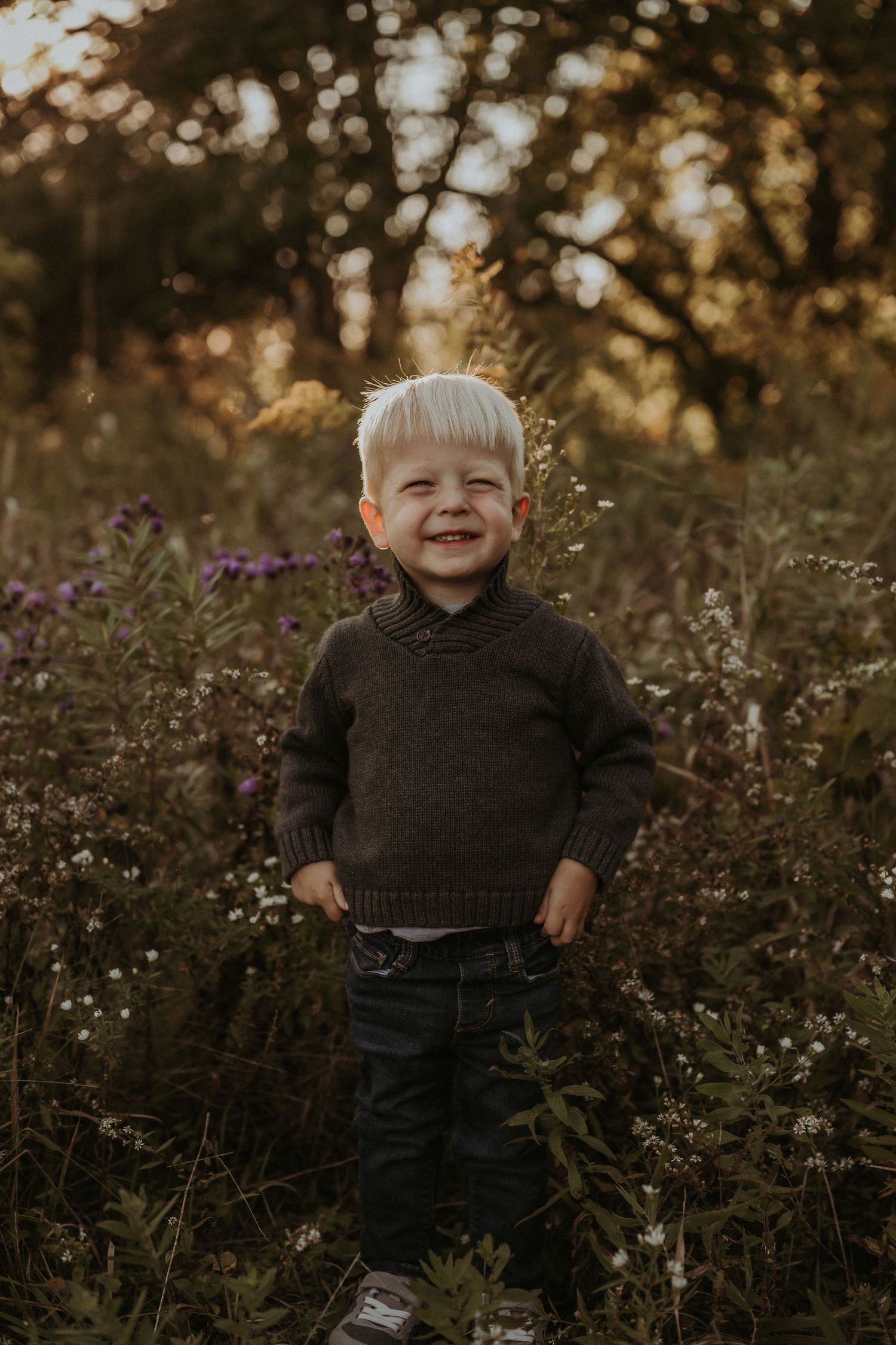 A cheerful figure in a dark sweater stands among wild autumn flowers at dusk.