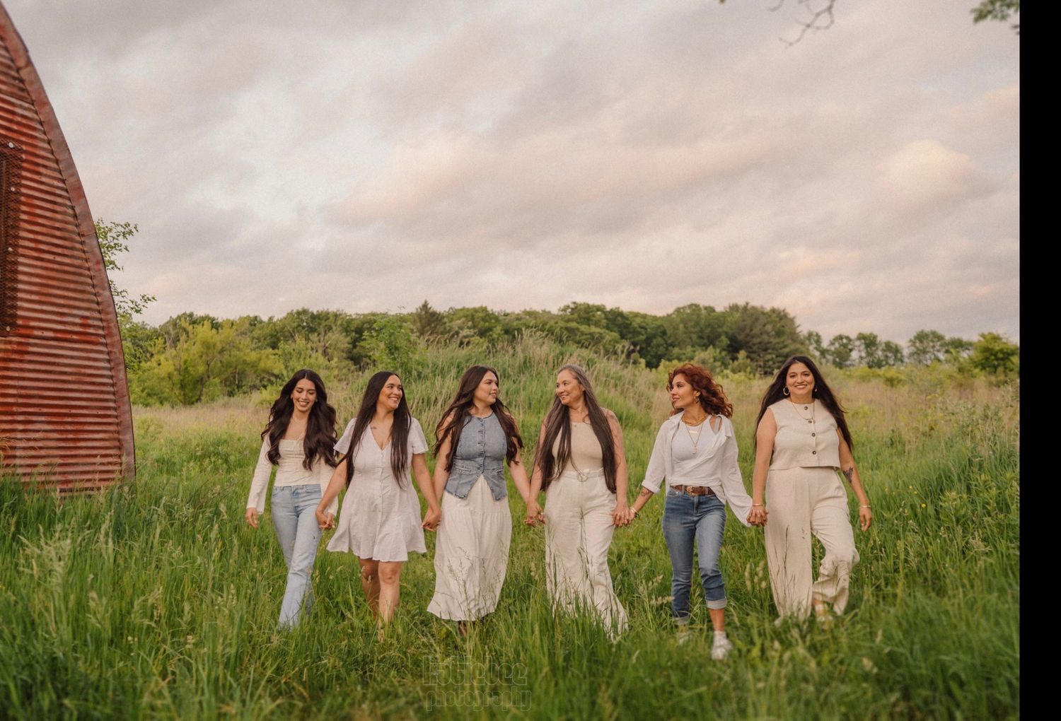 A group in light-colored clothing poses together near a red barn in a grassy field.