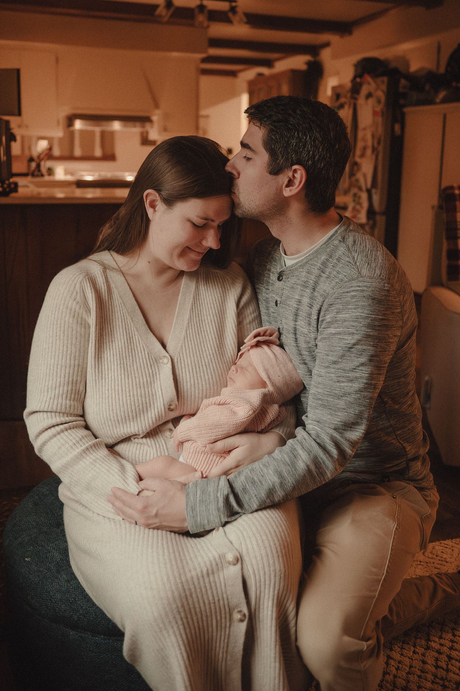 Family snuggling close together on couch in warm, intimate indoor lighting.