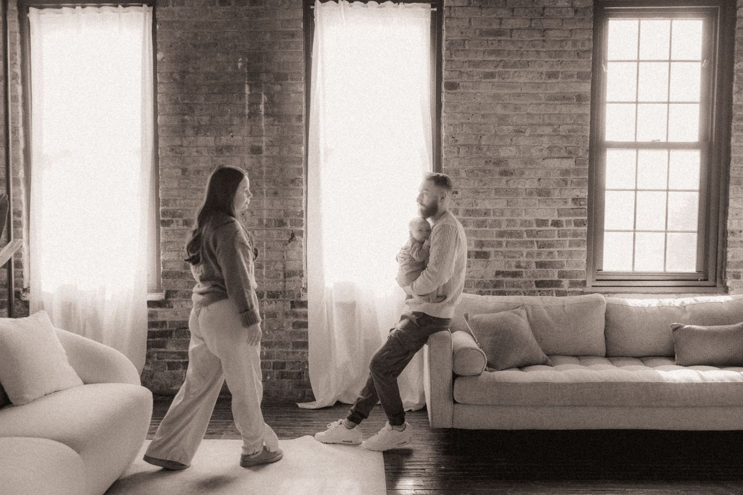 Monochrome photography in rustic brick interior with large windows.