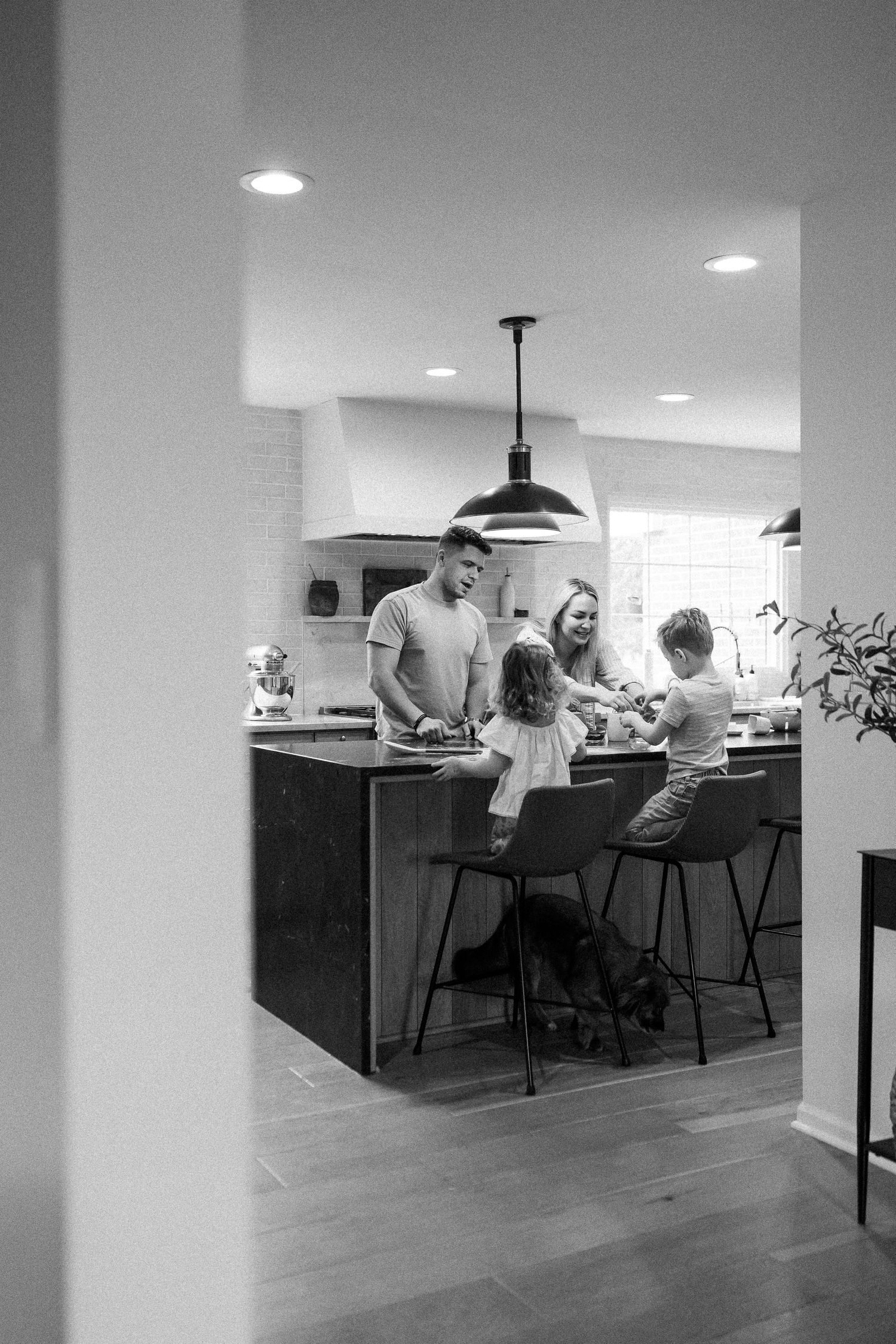 Black and white photo of a family gathered around a kitchen island, parents and two children enjoying time together.