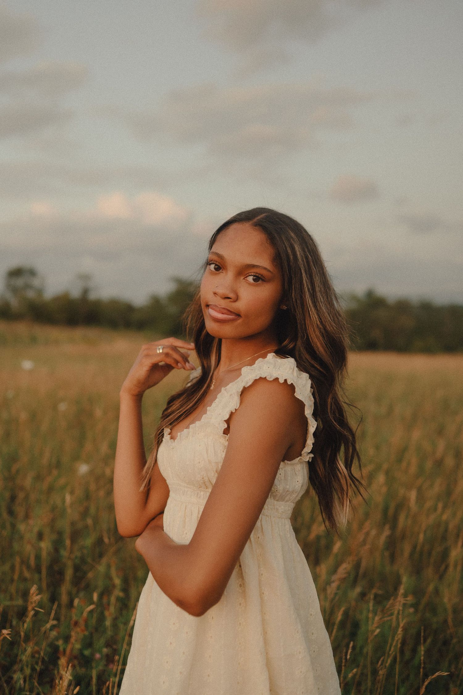 Young woman in white lace dress poses in a golden meadow during warm sunset light.