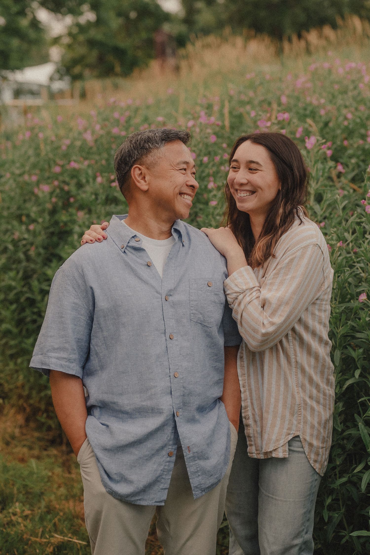 A smiling couple stands together in a lush garden, sharing a warm, joyful moment among blooming wildflowers.