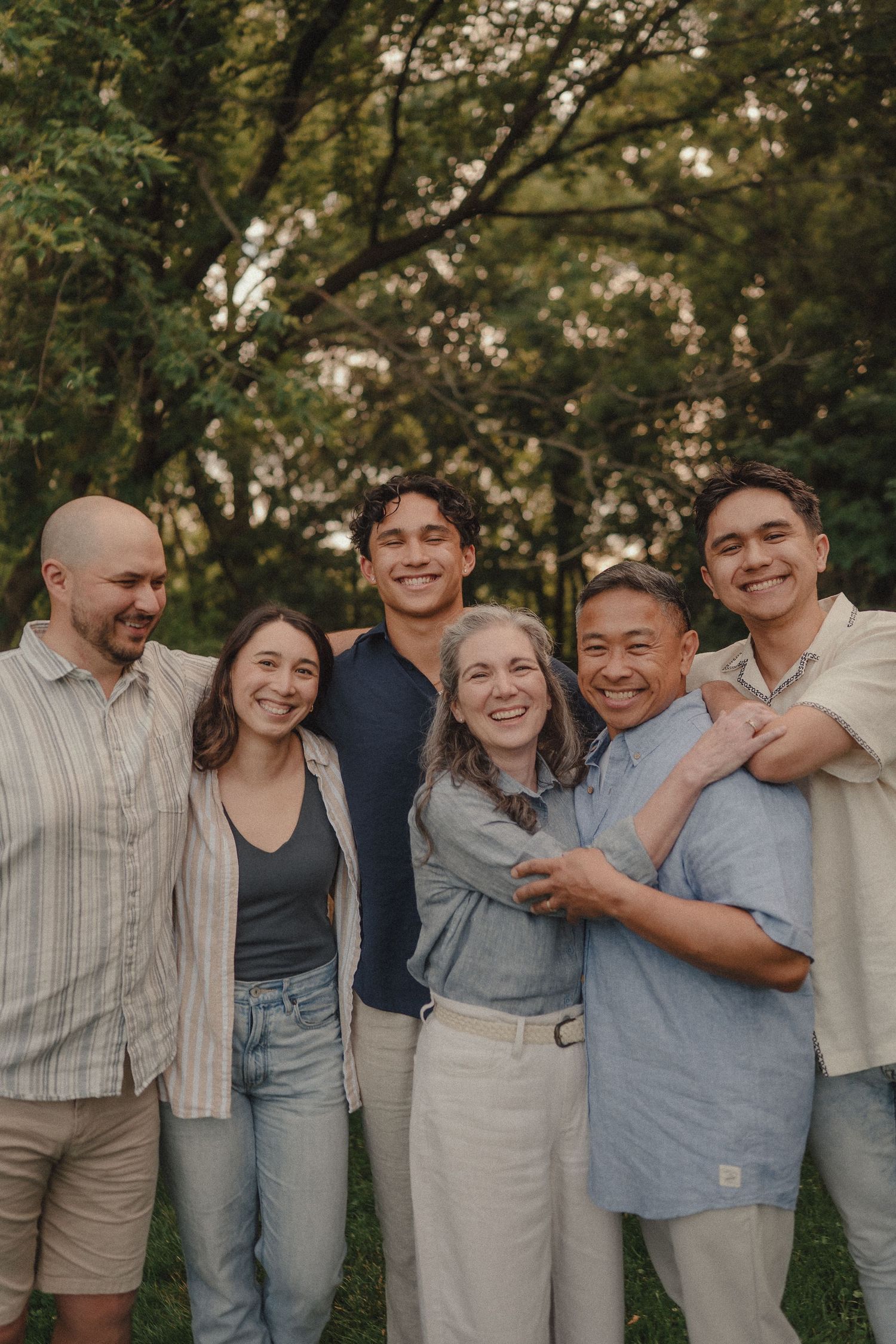 Smiling family of six hugging closely outdoors in a lush green park setting.