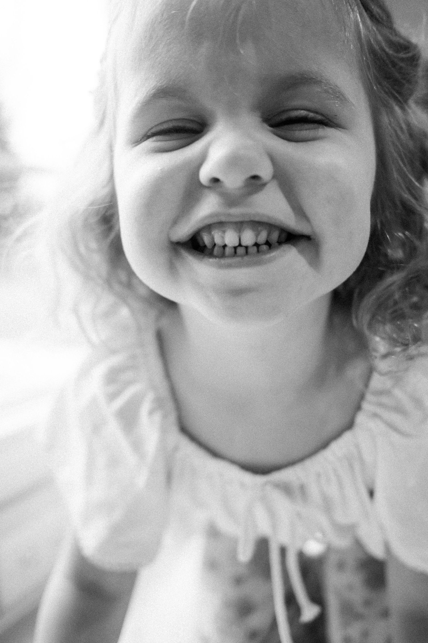 Happy young girl with curly hair smiling broadly in black and white portrait photo.