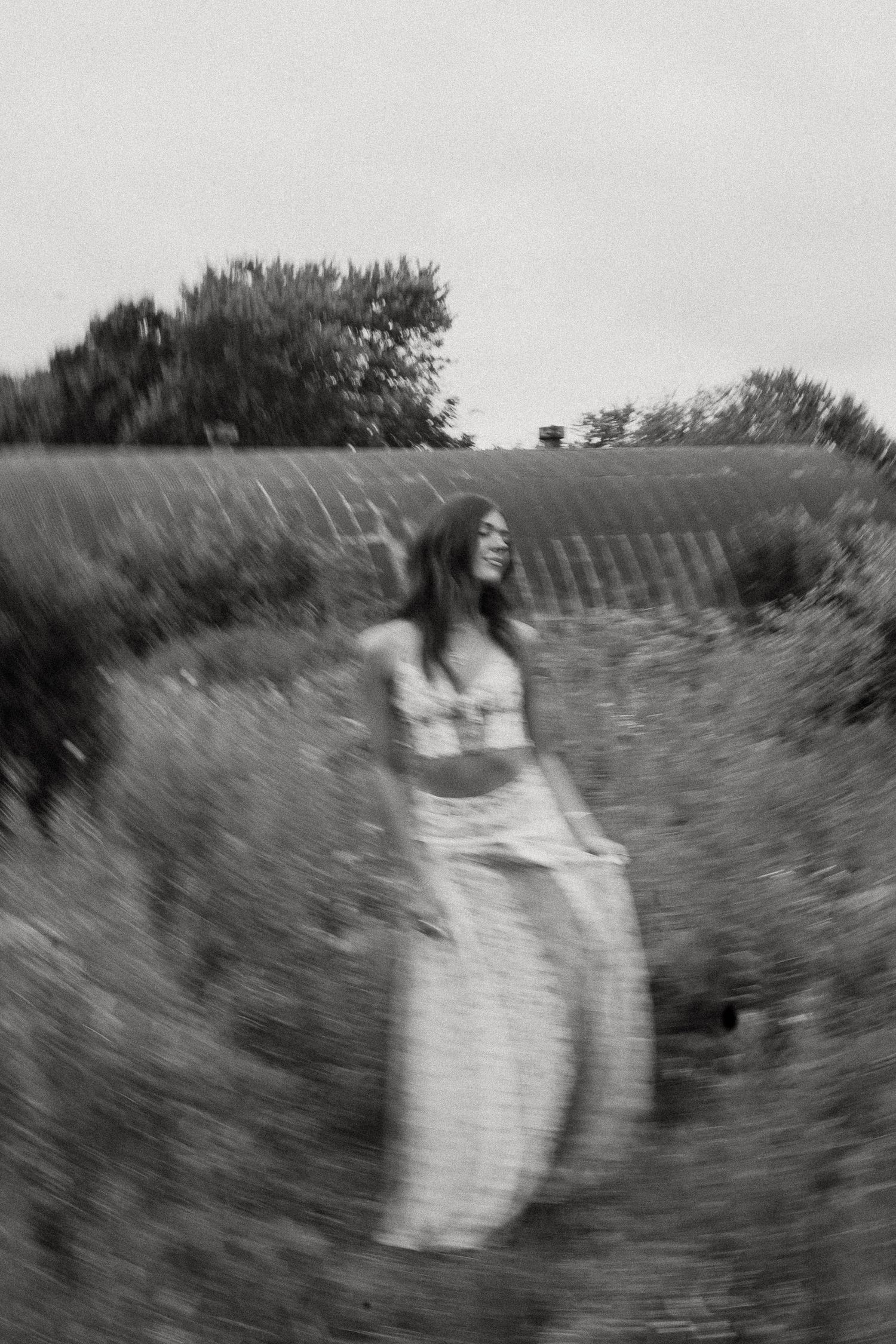 Black and white blurred photo of a woman in a floral dress walking through a lavender field.