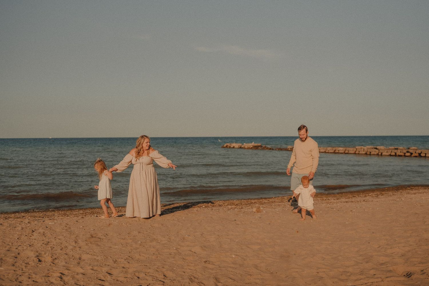 Family of four enjoying a sunset beach walk on sandy shore with calm ocean waters in the background.