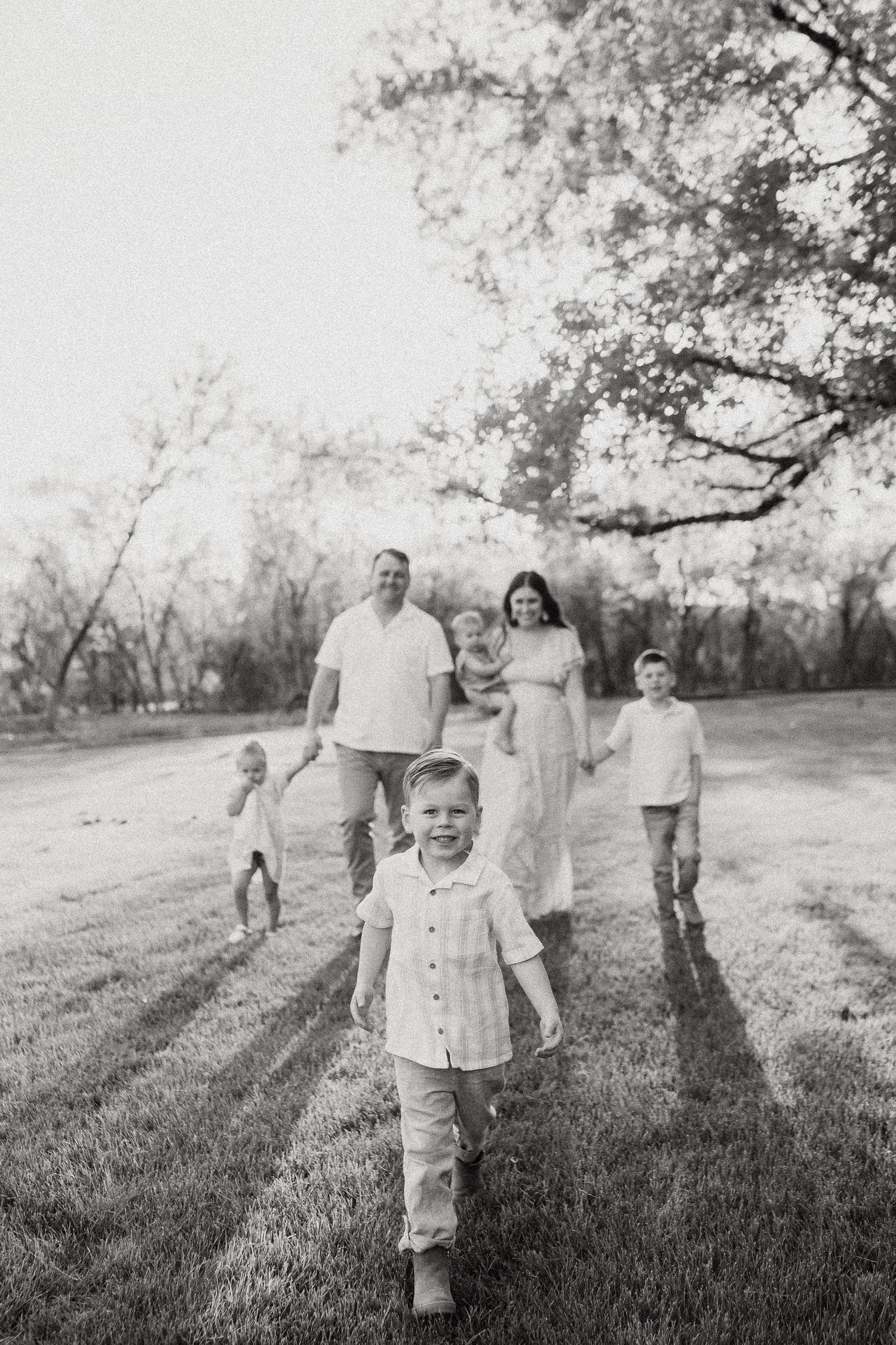 Black and white photo of a family walking through a grassy field toward the camera at sunset.