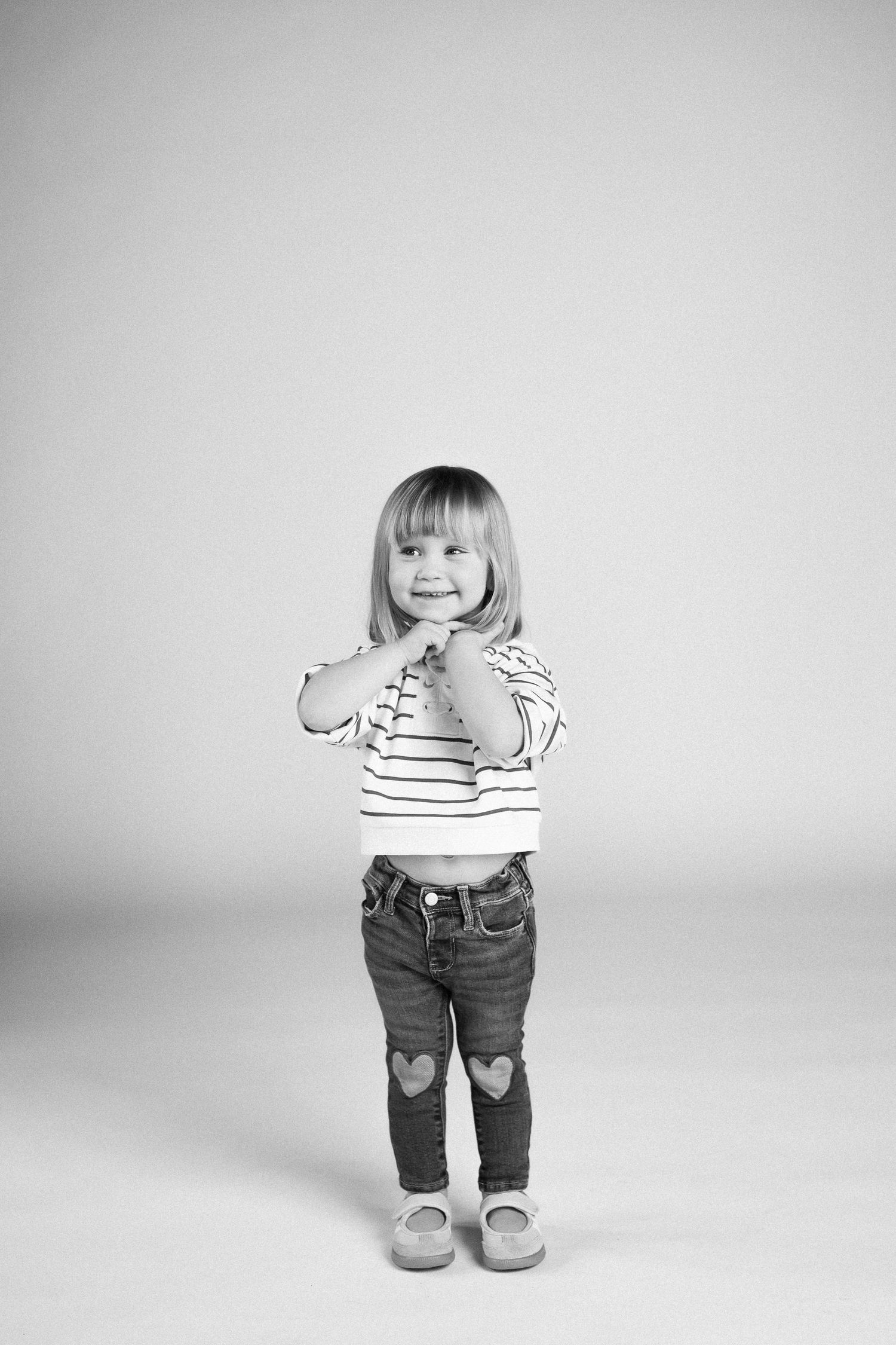 Black and white sequence shows a toddler in striped shirt and jeans sitting and standing against white backdrop.