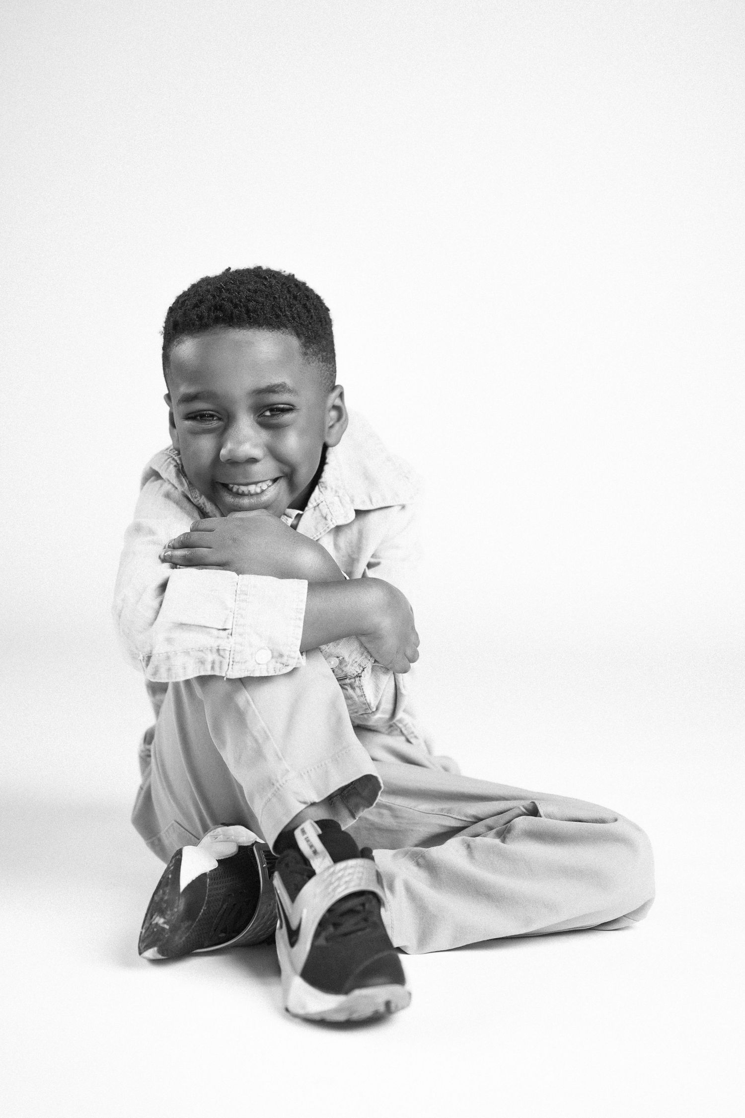 Black and white photos of a child in white clothing sitting and posing playfully on the floor.