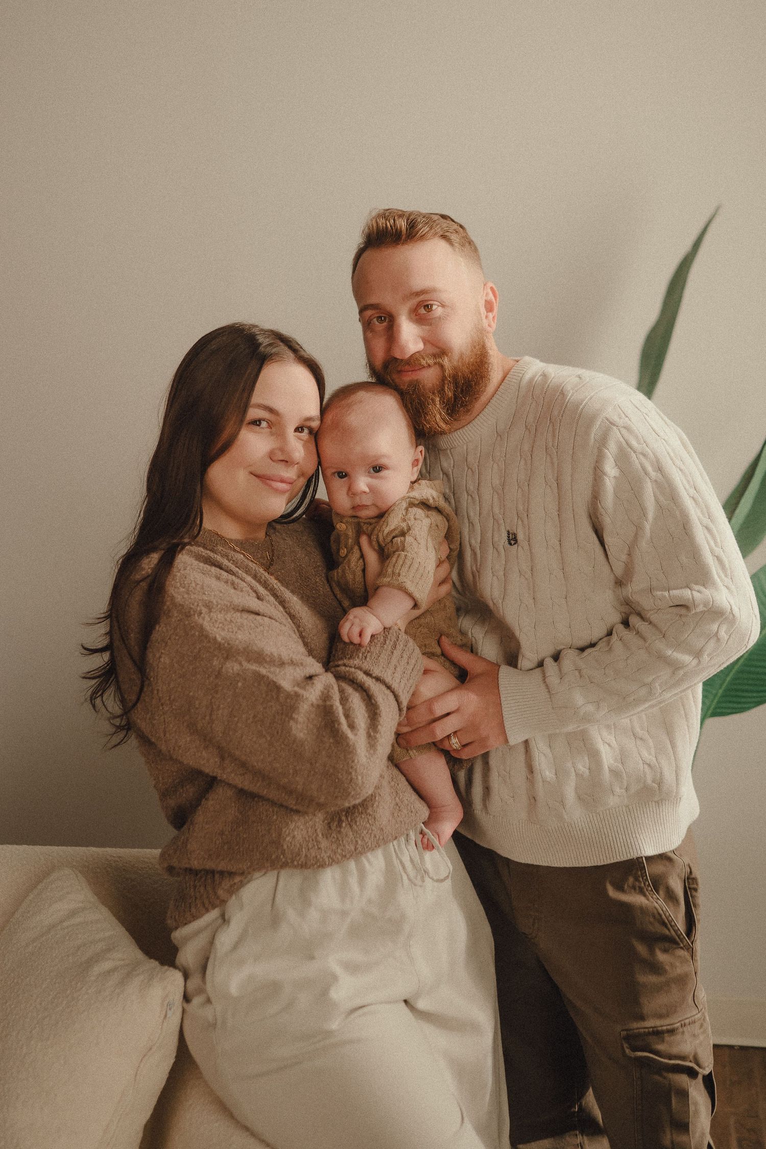 A family shares tender moments together in a series of warm-toned photos against a neutral wall.