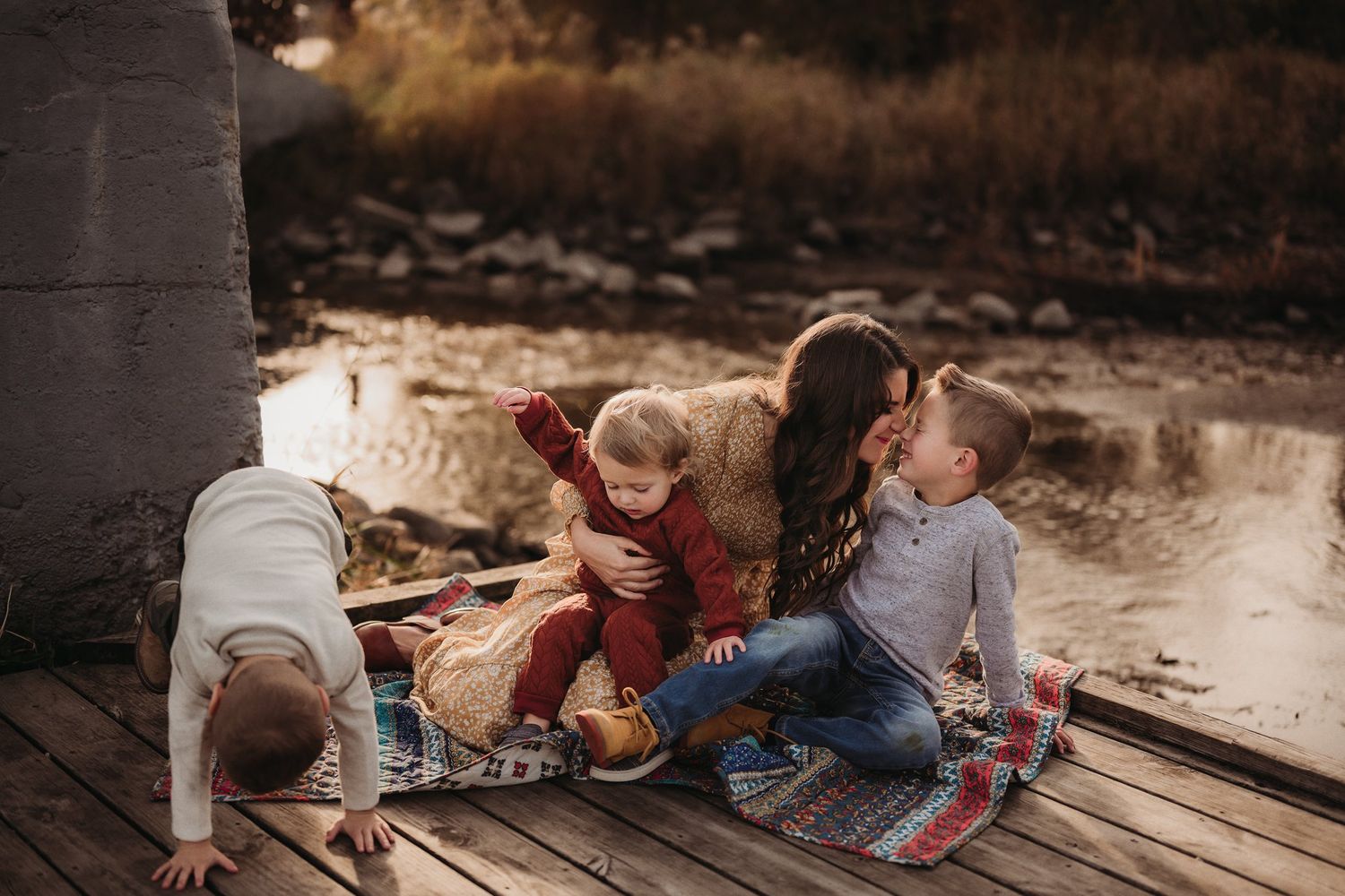 A family plays together on a blanket on a wooden dock during golden hour.