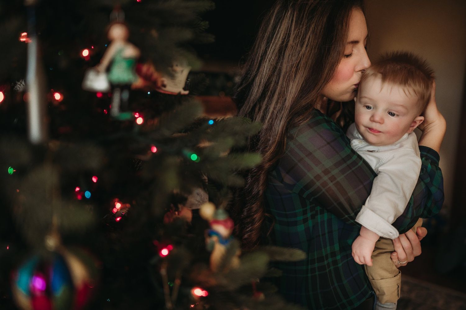 A cozy Christmas scene with colorful lights as a parent holds a baby near a decorated tree.