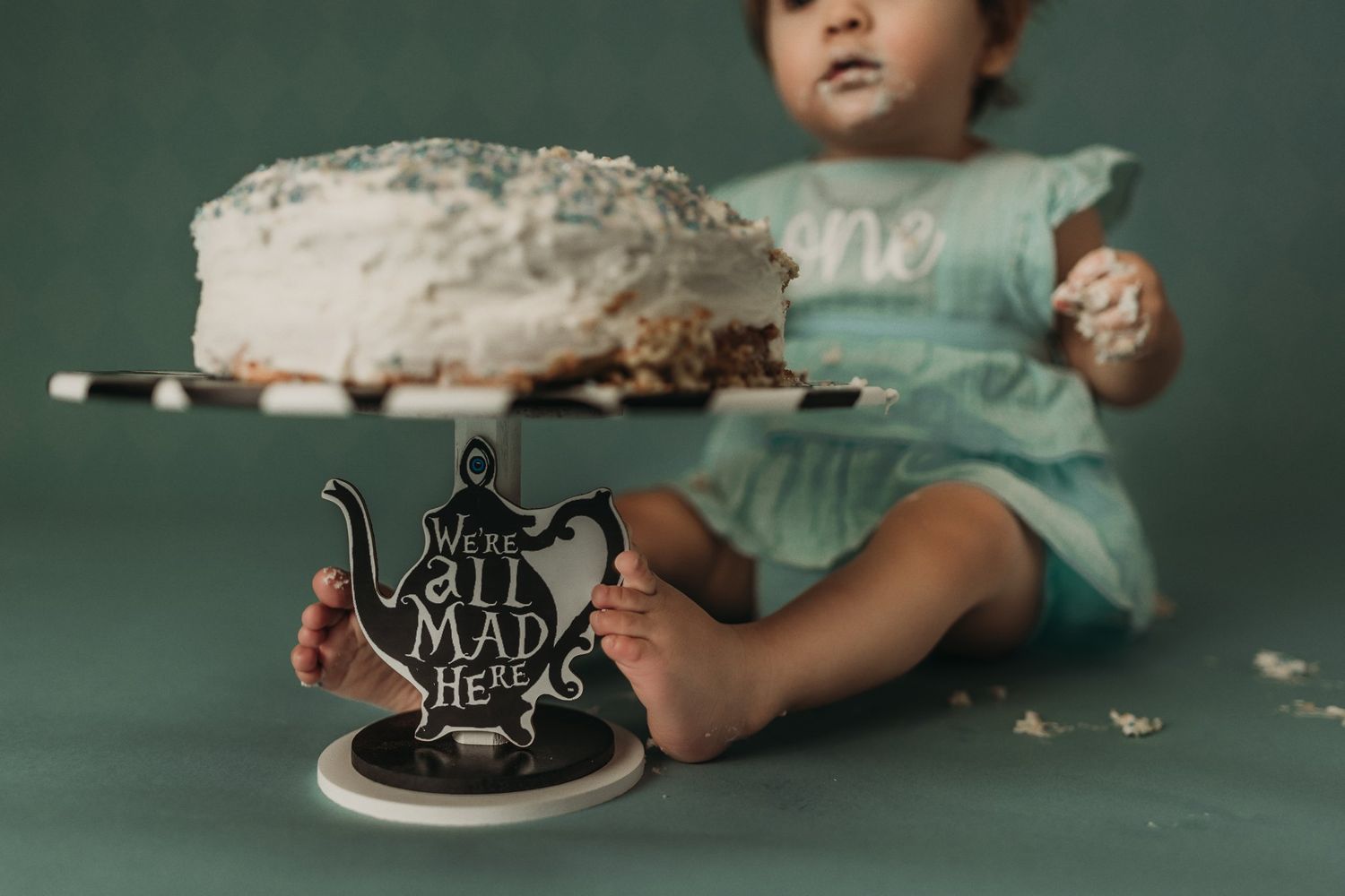 Detail shot of a decorative cake stand with 'EAT ME' text and scattered cake crumbs.
