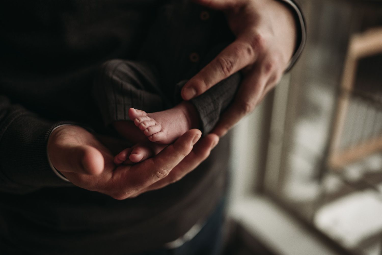 Close-up of gentle hands cradling a tiny sleeping newborn in dim lighting.