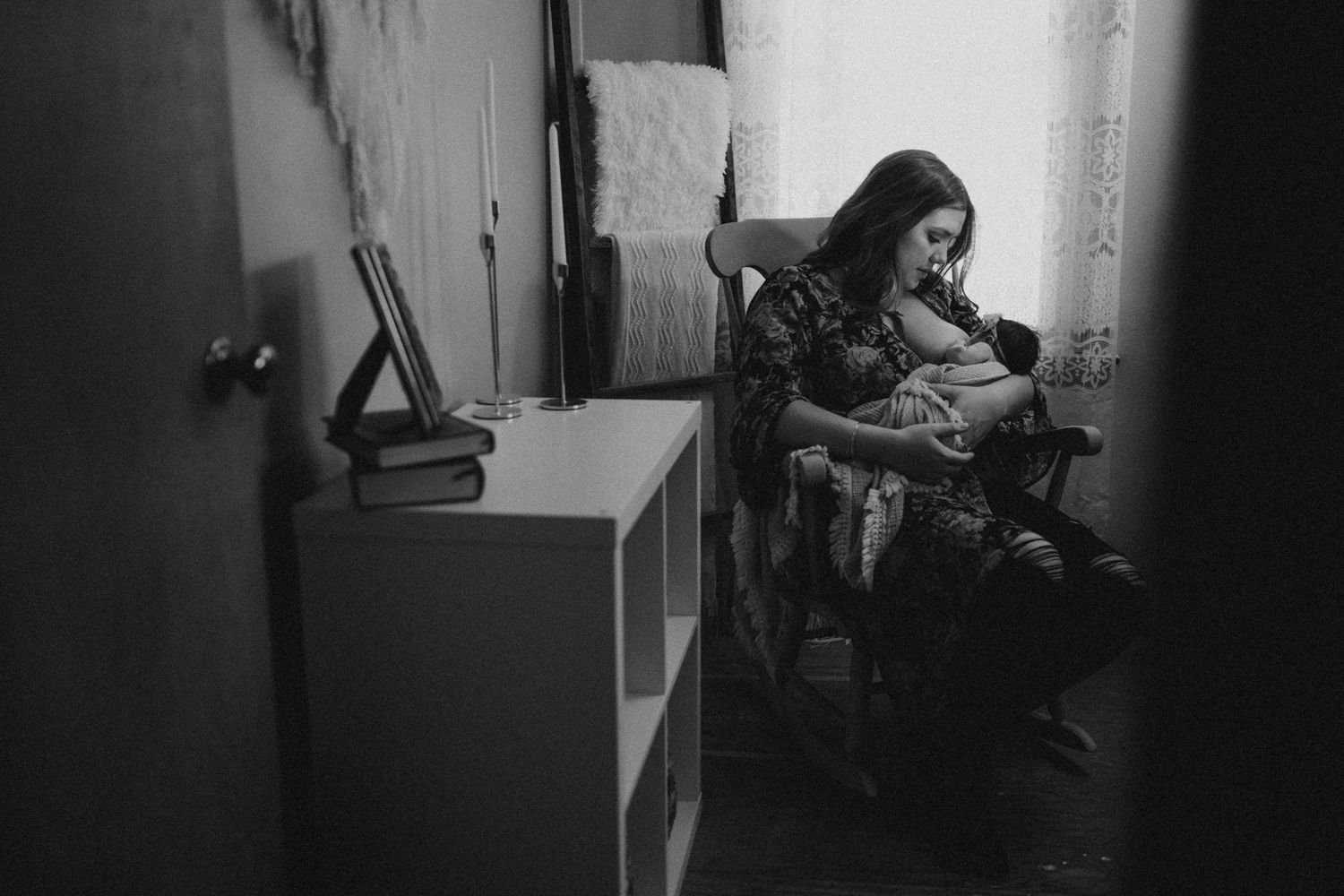 Black and white image showing a nursery room with a rocking chair by a window.