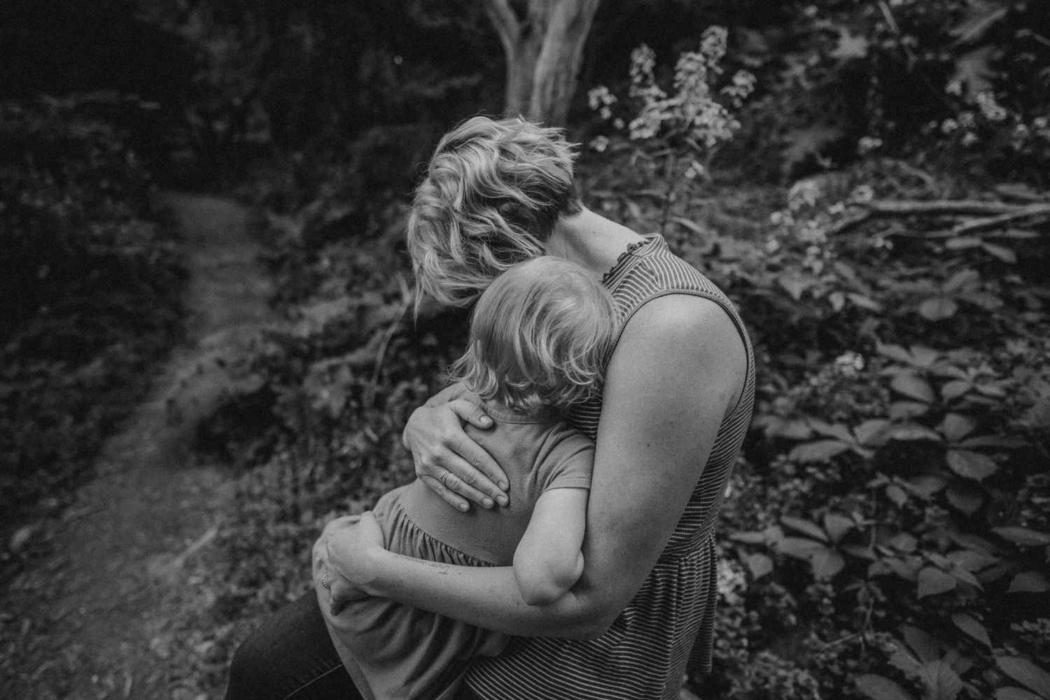 Intimate black and white portrait of tender embrace outdoors among flowering bushes.