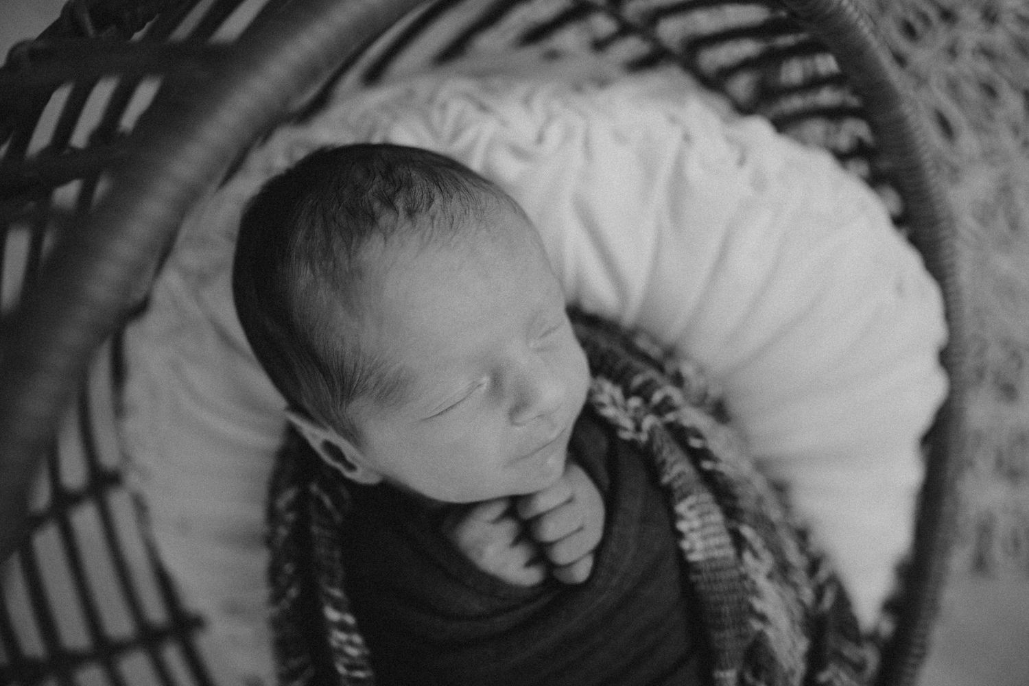A black and white overhead shot of a sleeping newborn in a basket.