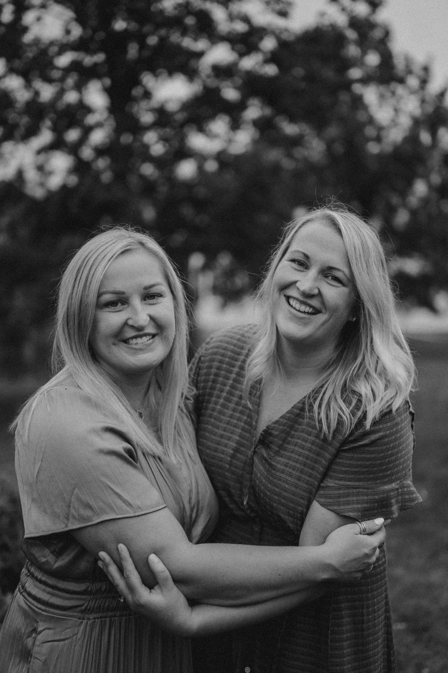 Black and white portrait of two women laughing and embracing outdoors.
