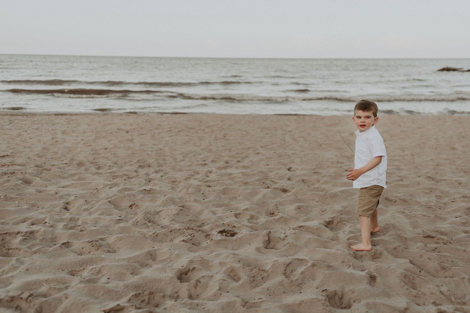 A small child in white shirt and khaki shorts runs alone on a beach.