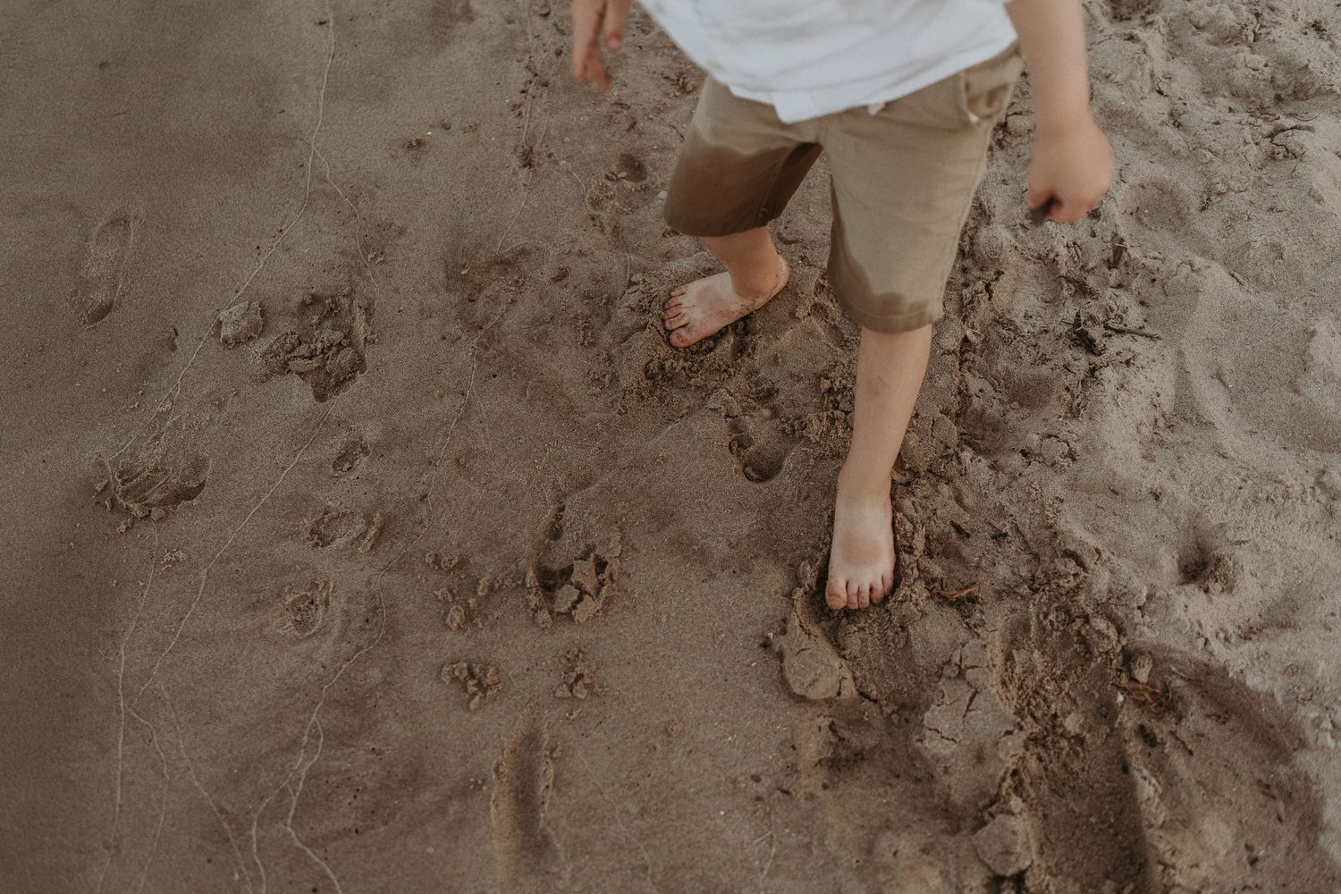 Close-up of feet making footprints in wet beach sand.