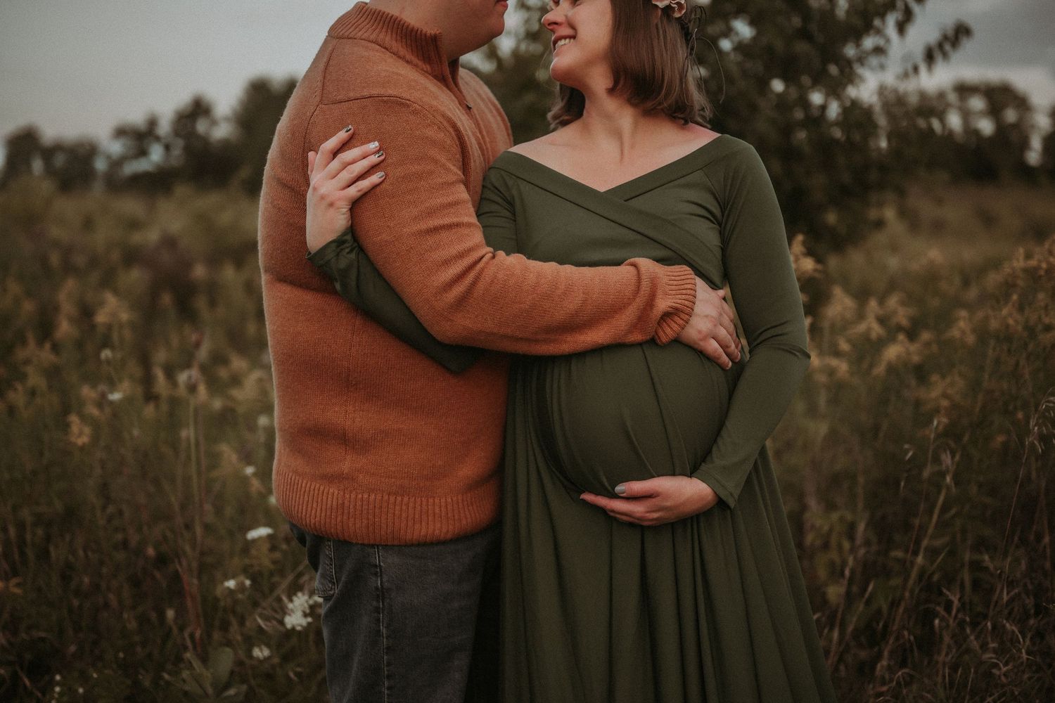 Close-up maternity photo showing couple's tender embrace in autumn field.