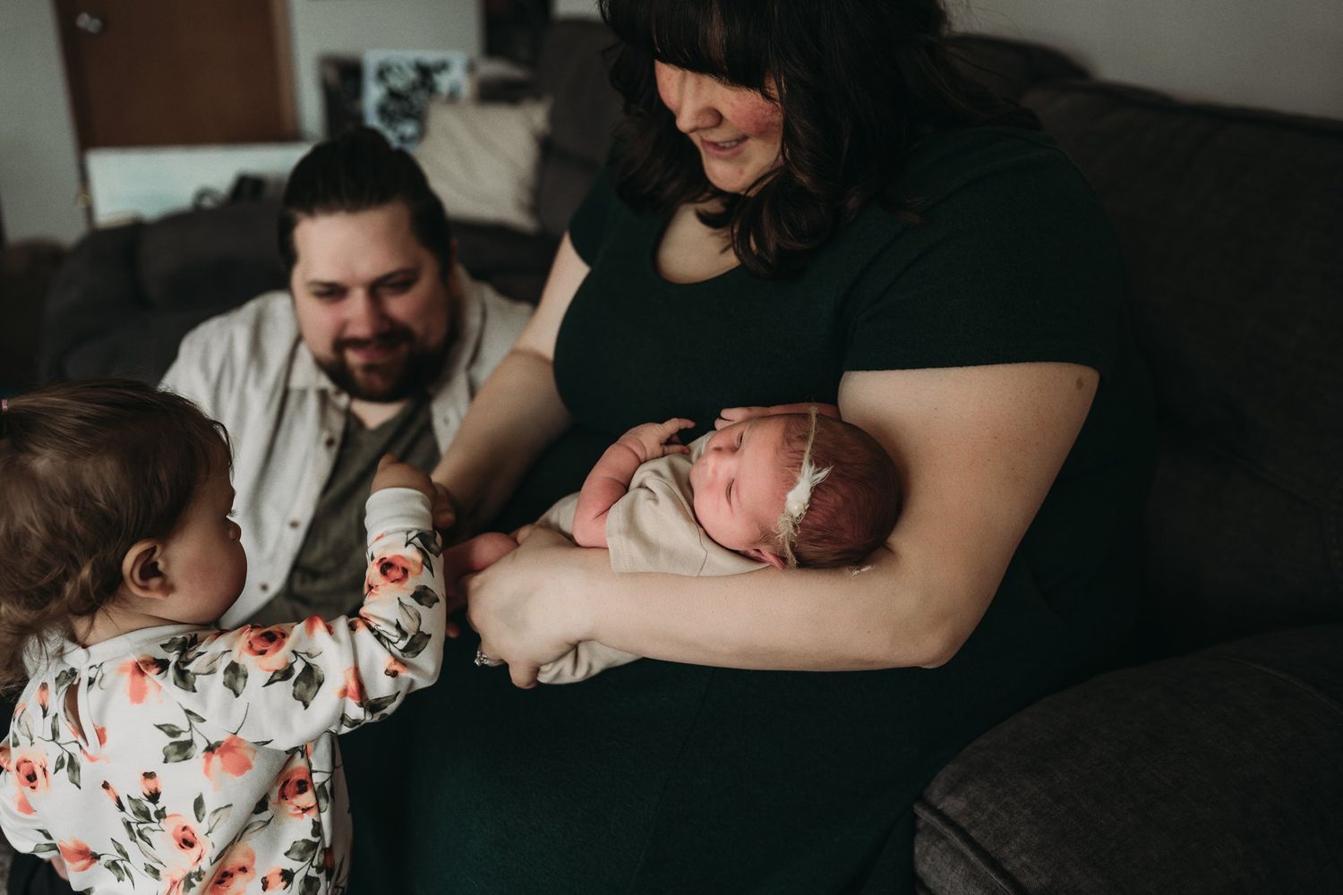 Family gathered on couch with newborn as toddler reaches out to touch.