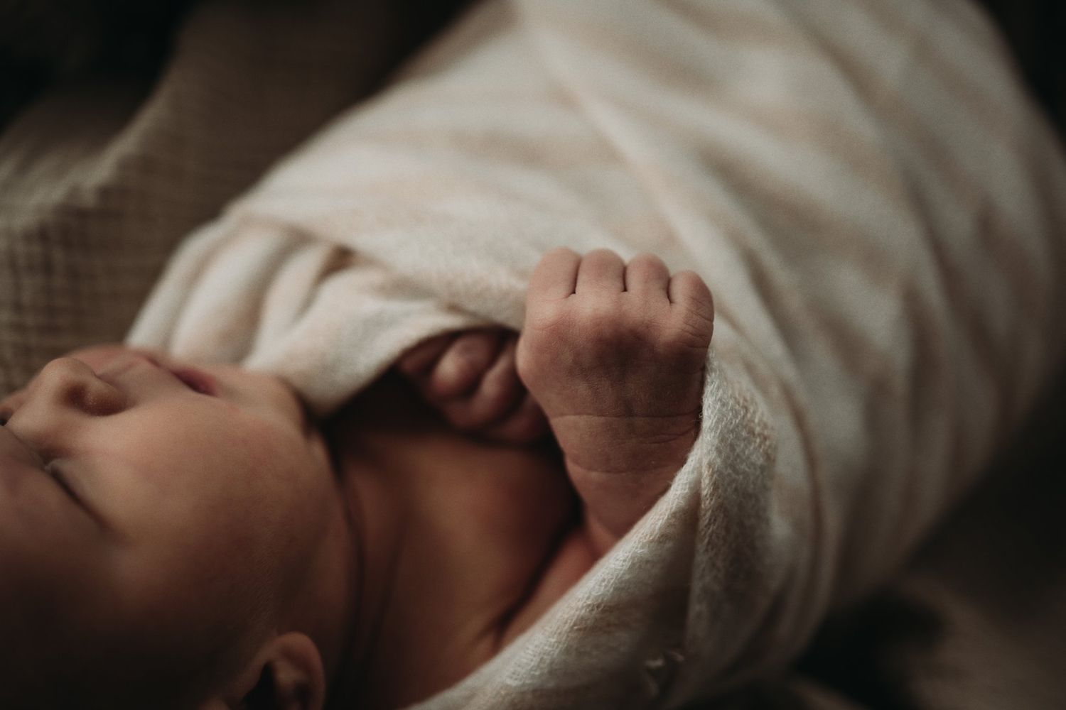 Delicate close-up of sleeping infant's hand grasping soft white fabric.
