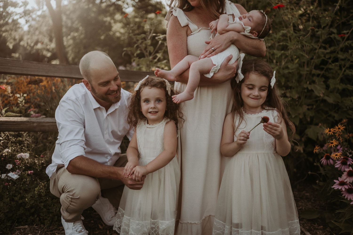 A sunset family portrait in a garden with everyone dressed in coordinating white and cream outfits.