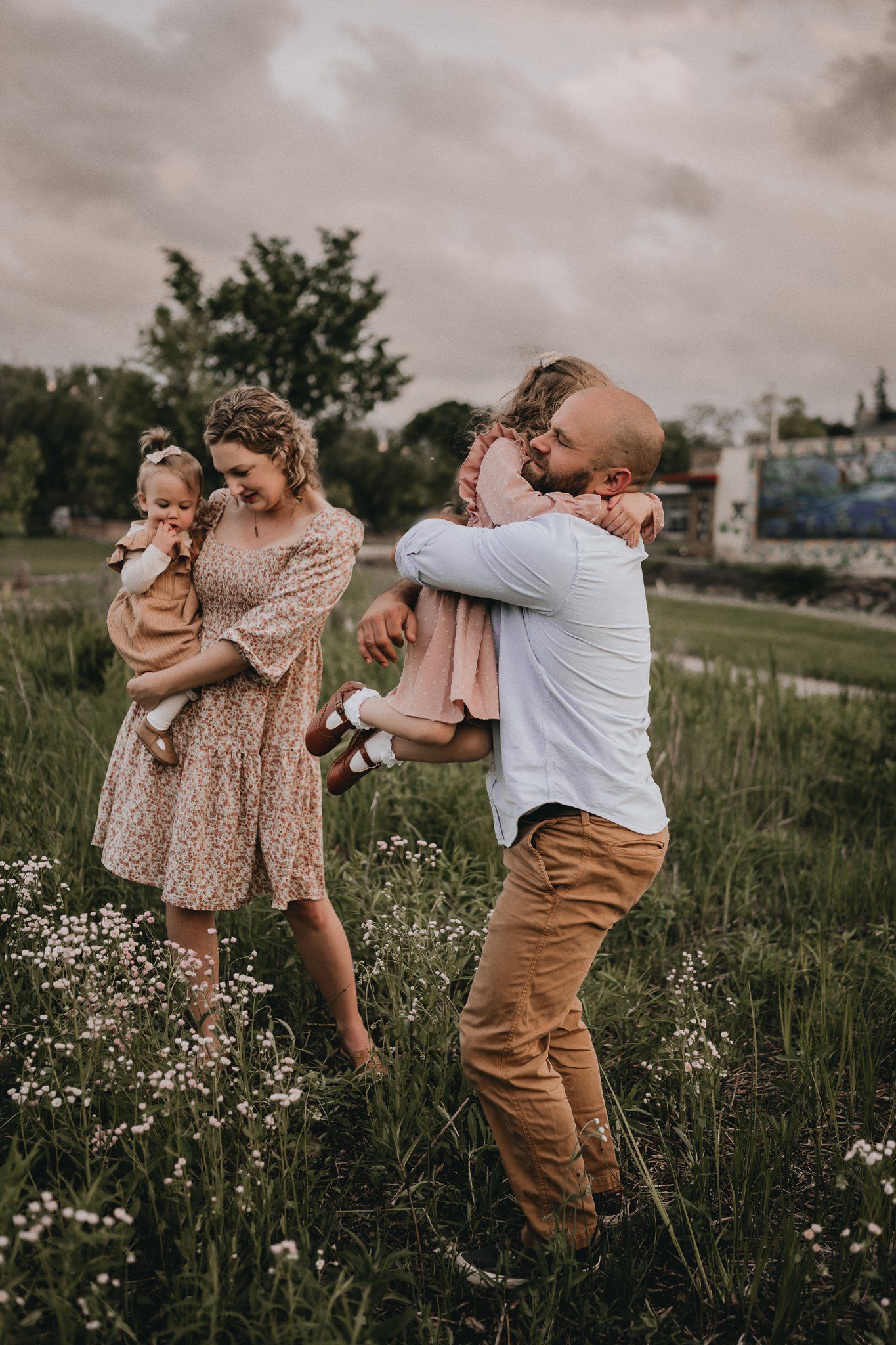 A family shares playful moments together in a field of blooming daisies at dusk.