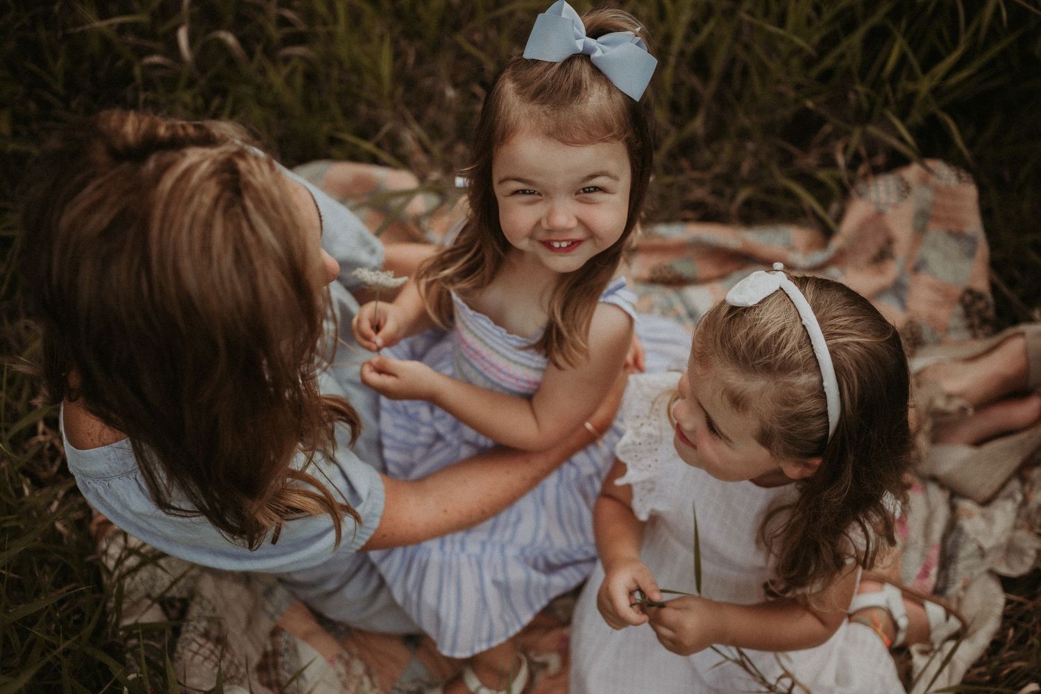 Three people sharing joyful laughter while sitting on a blanket outdoors.