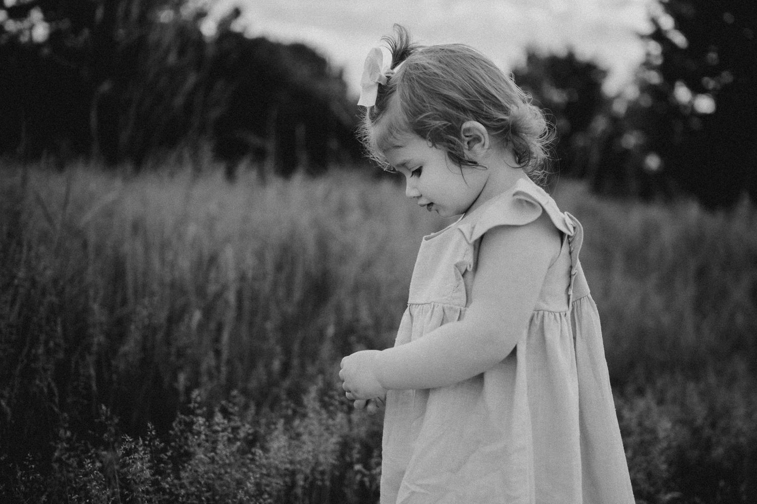 A quiet moment captured in black and white of a child examining something in a meadow.
