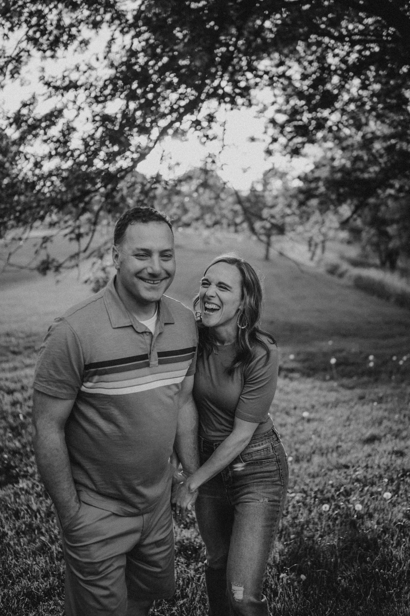 Black and white photo of a laughing couple enjoying a candid moment outdoors.