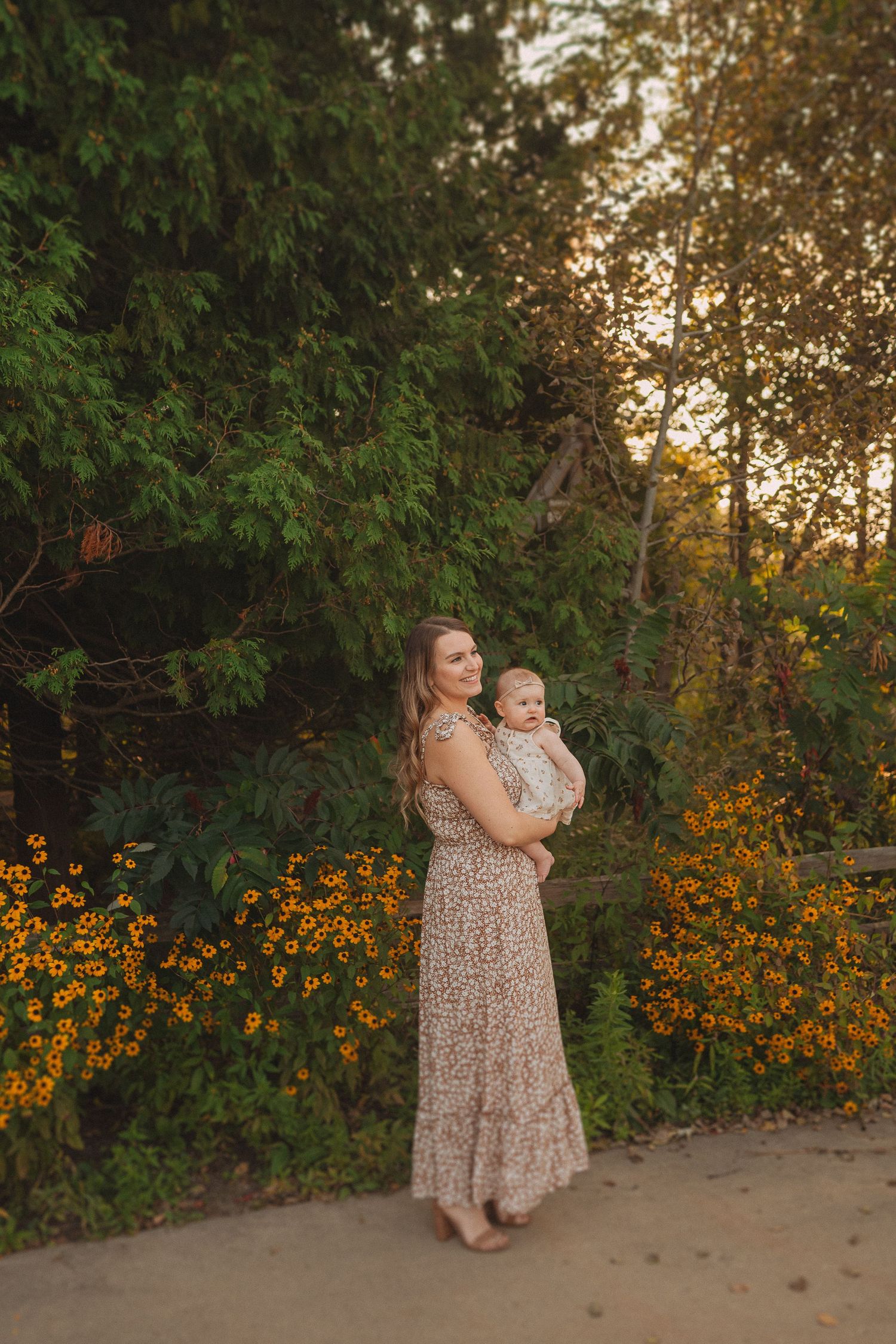 A long floral dress silhouette stands against a garden backdrop of orange flowers at golden hour.